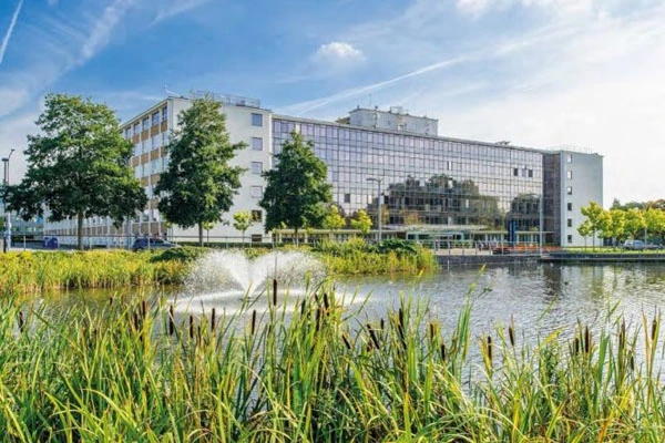 Modern waterfront buildings with glass and white facades beside a pond with reeds and green vegetation