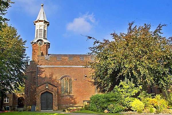 Red brick church with white wooden steeple, arched doorway and window, surrounded by green foliage and trees