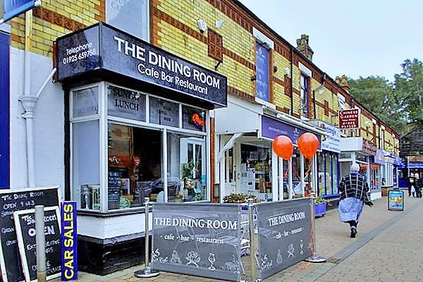 Row of brick buildings with shop fronts, including "The Dining Room" café and restaurant with orange lanterns