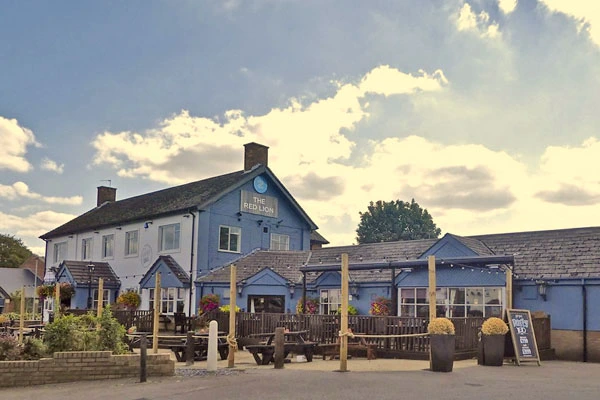 Blue-painted pub building with wooden pergola seating area, planters, and signage in front