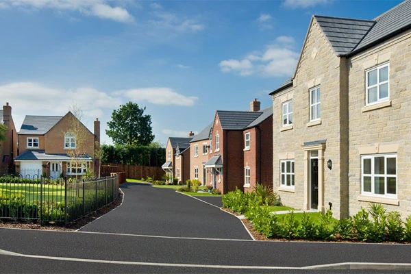 Row of new-build houses along a residential street with stone and brick facades, manicured gardens, and clear blue sky