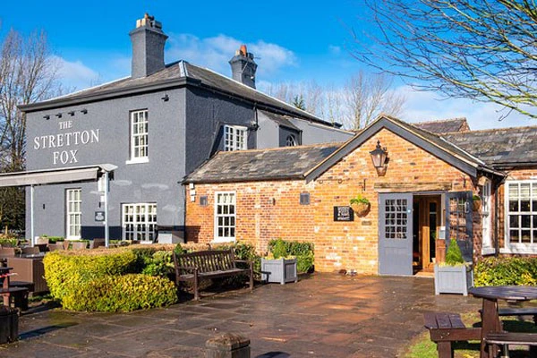 The Stretton Fox pub, a grey and brick building with chimneys, viewed from the courtyard with benches and planters