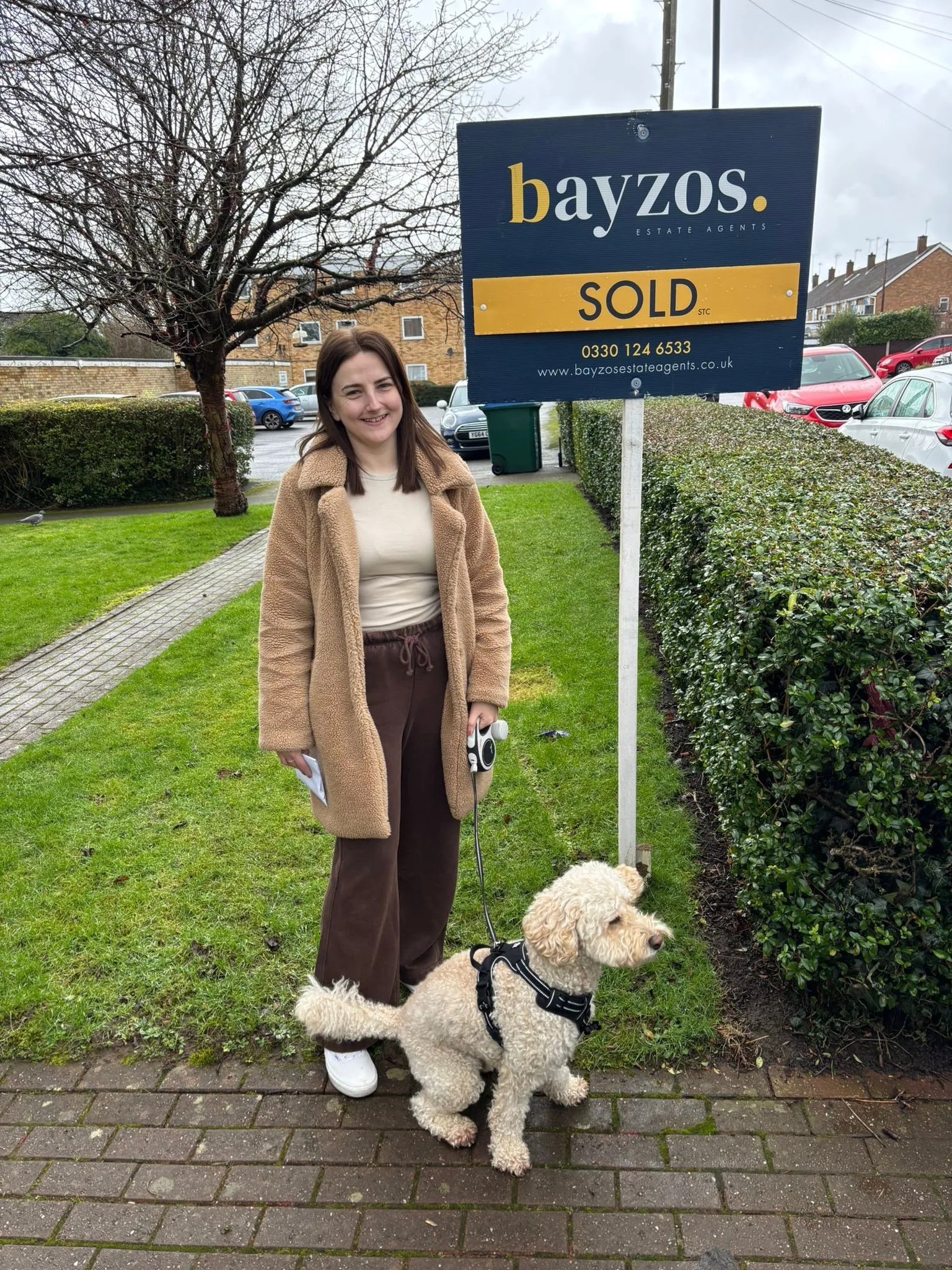 A homeowner and their dog stand next to a bayzos estate agents sold board on an estate in Coventry