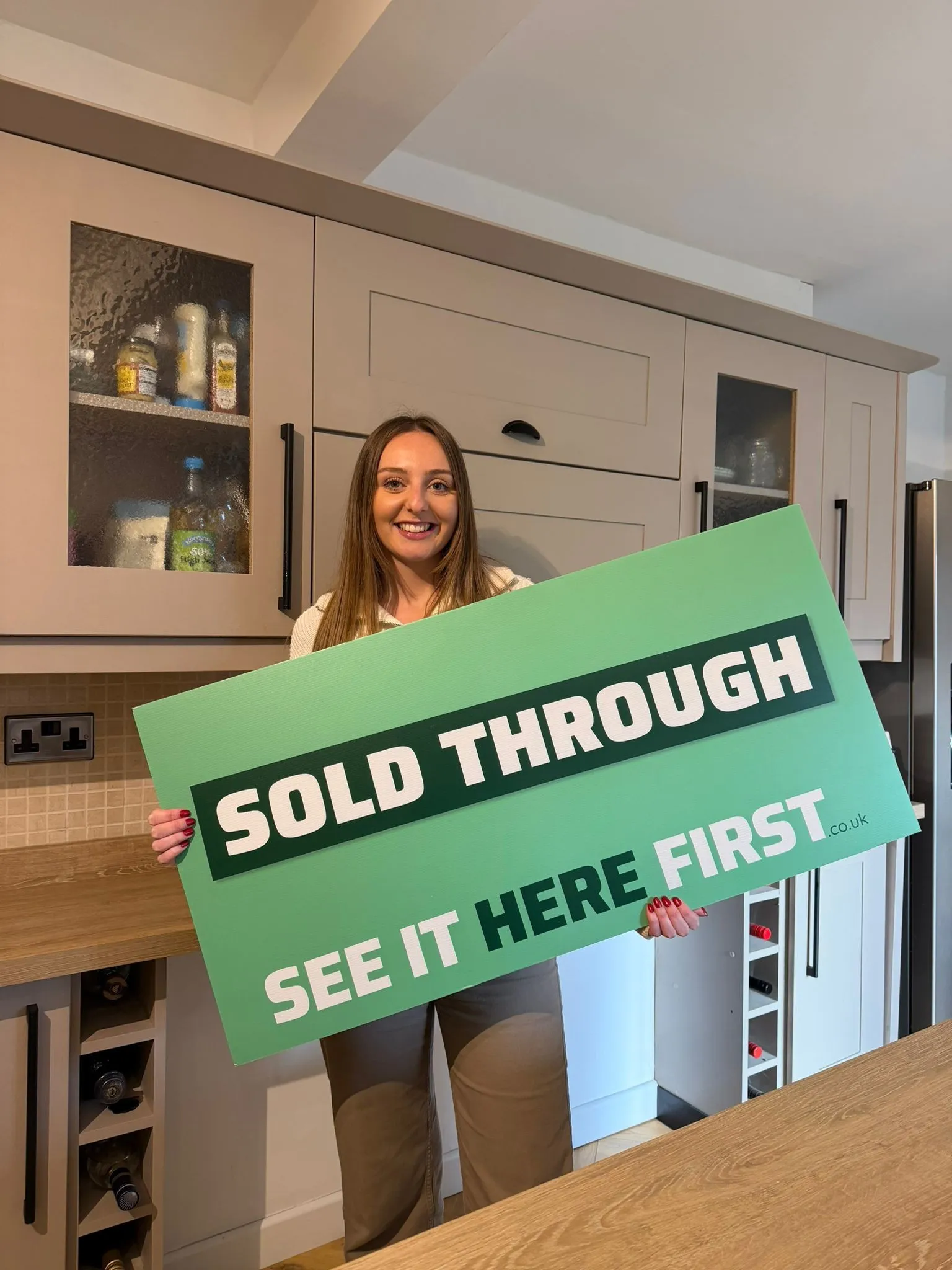 A smiling homeowner holds a board saying sold through see it here first