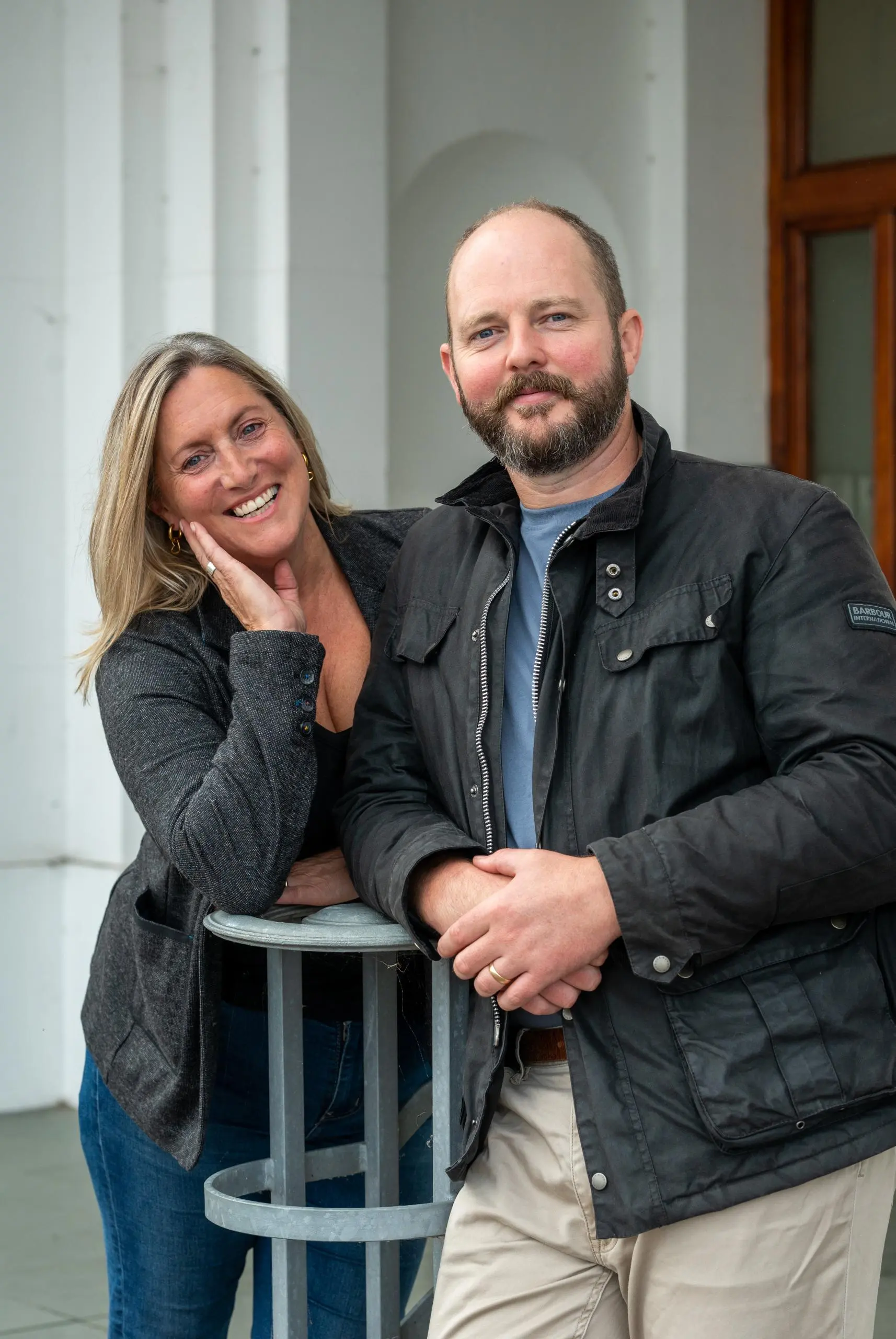 Two people posing together outside a building with white columns and a wooden door