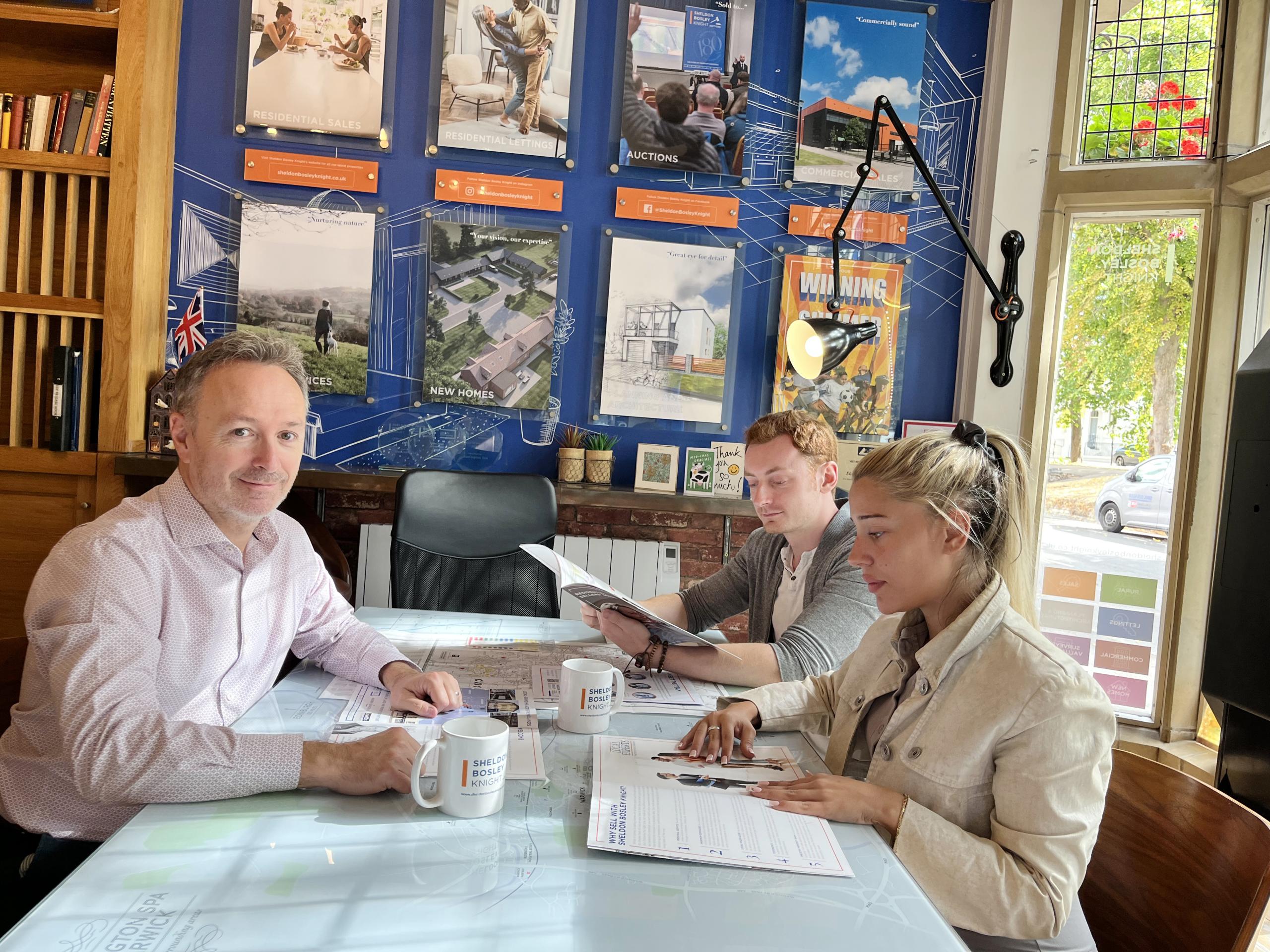 A Sales Valuer for Sheldon Bosley Knight sits at a table with a couple of home buyers