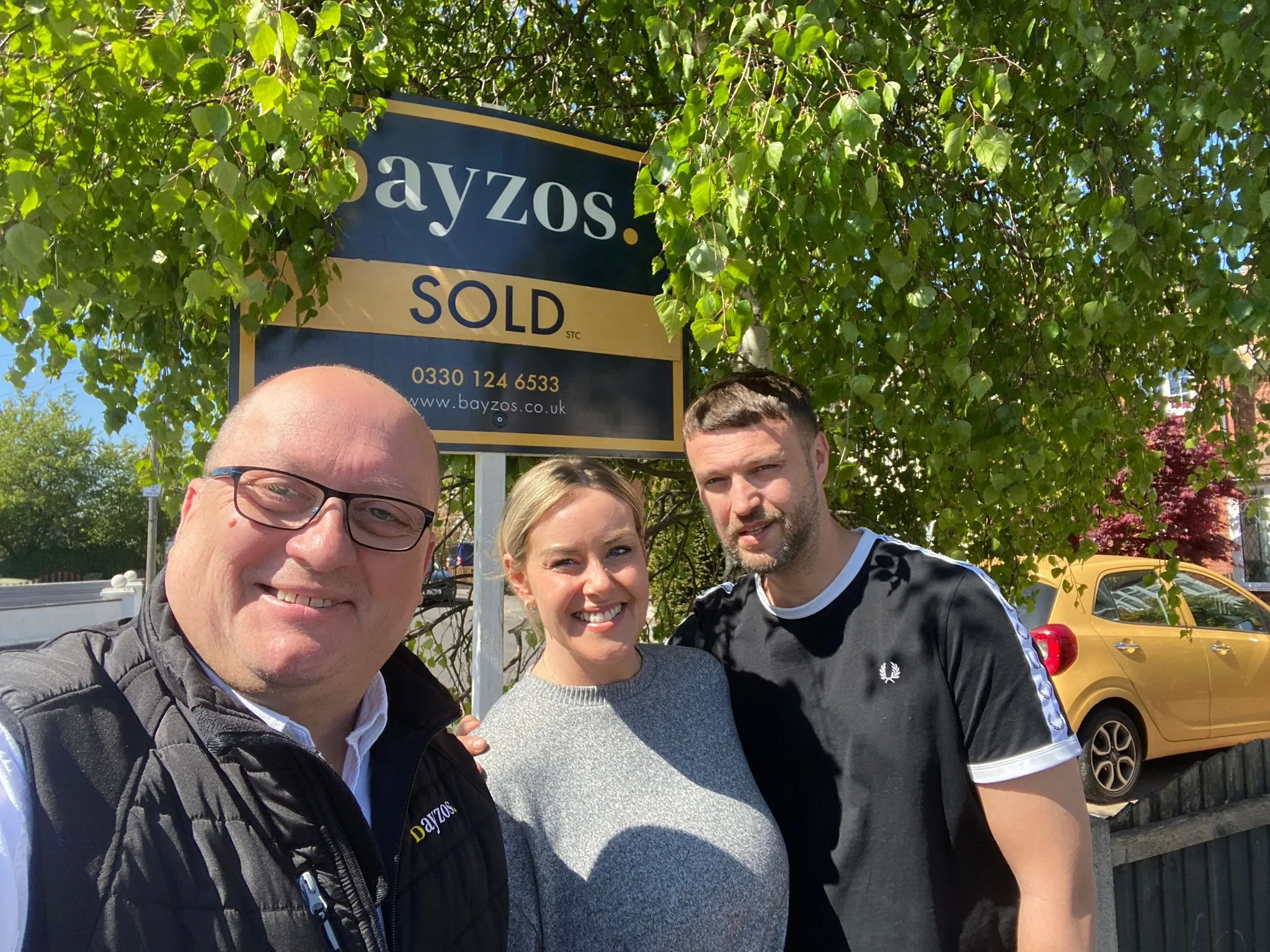James from Bayzos estate agents standing with two homeowners in front of a sold board