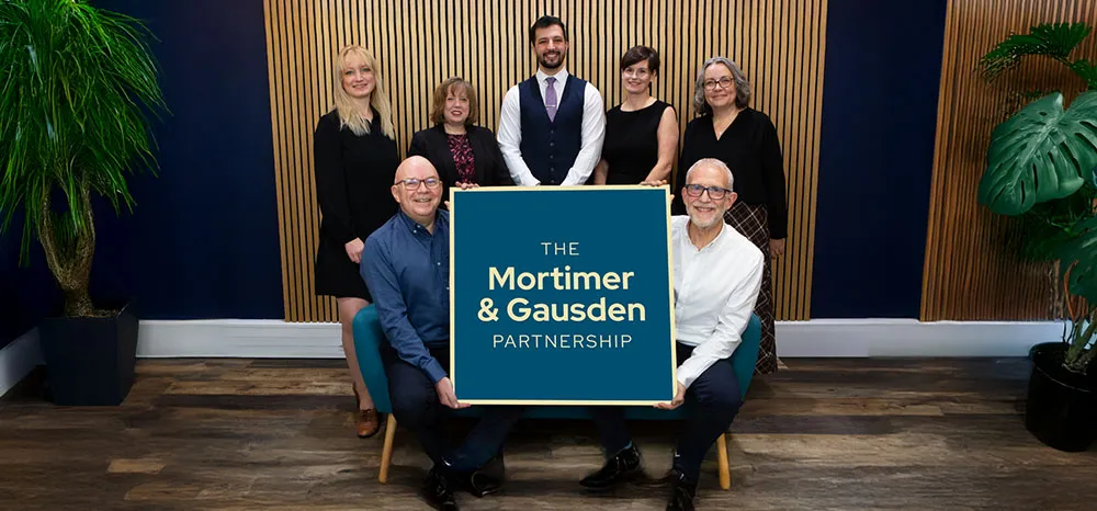 Mortimer & Gausden Partnership team holding sign in office