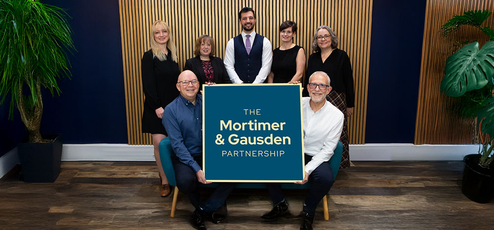 Mortimer & Gausden Partnership team holding sign in office
