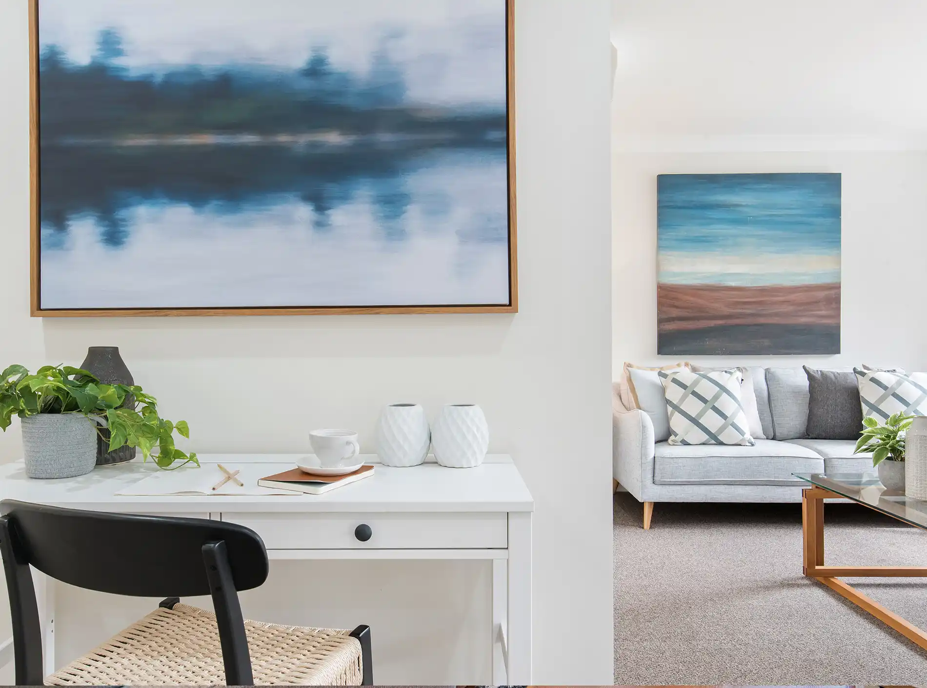 Modern living room with grey sofa, framed landscape paintings, potted plants, and wooden coffee table