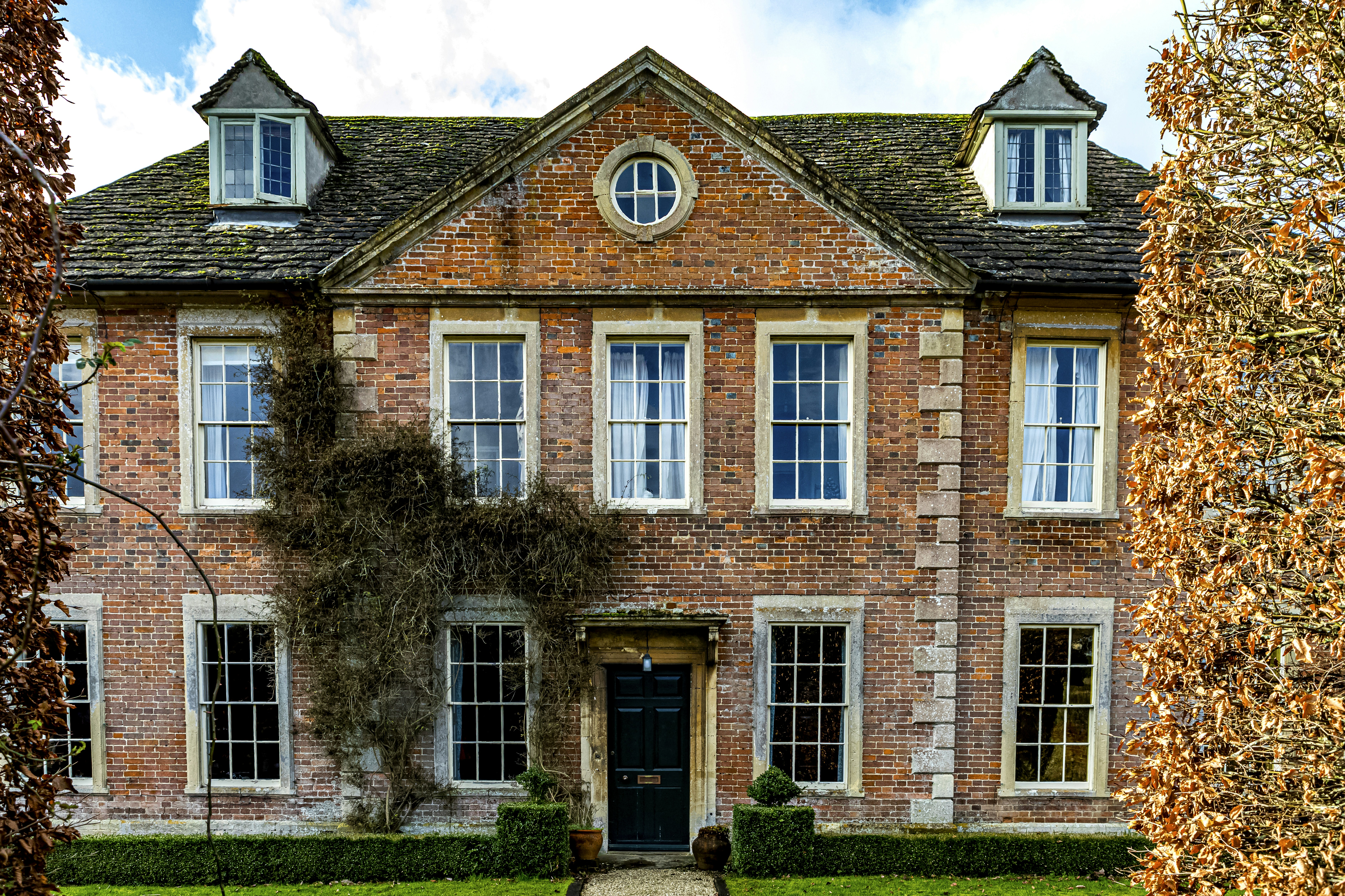Historic Lacock village cottage with traditional brick architecture, thatched roof, and manicured gardens