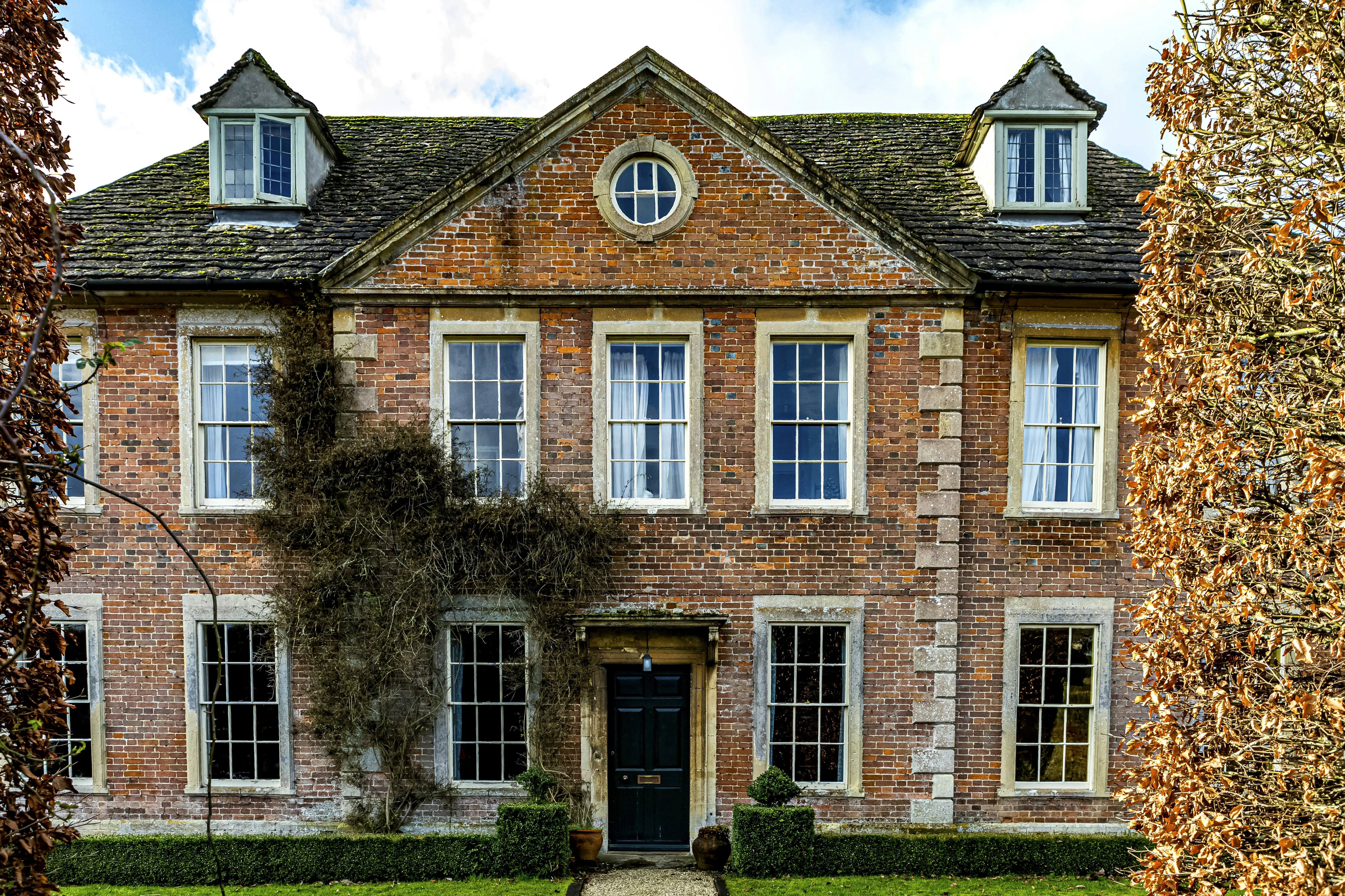 Historic Lacock village cottage with traditional brick architecture, thatched roof, and manicured gardens