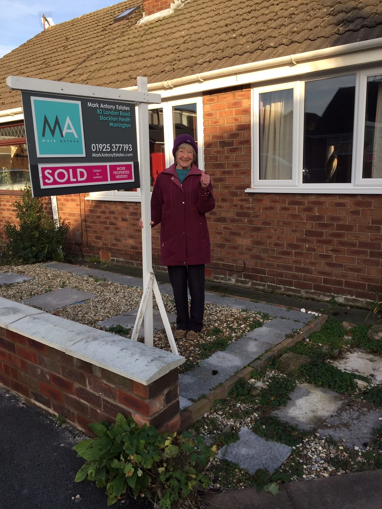 Person standing next to a "SOLD" estate agent board for Mark Antony Estates, 82 London Road, Stockton Heath, Warrington, outside a brick bungalow