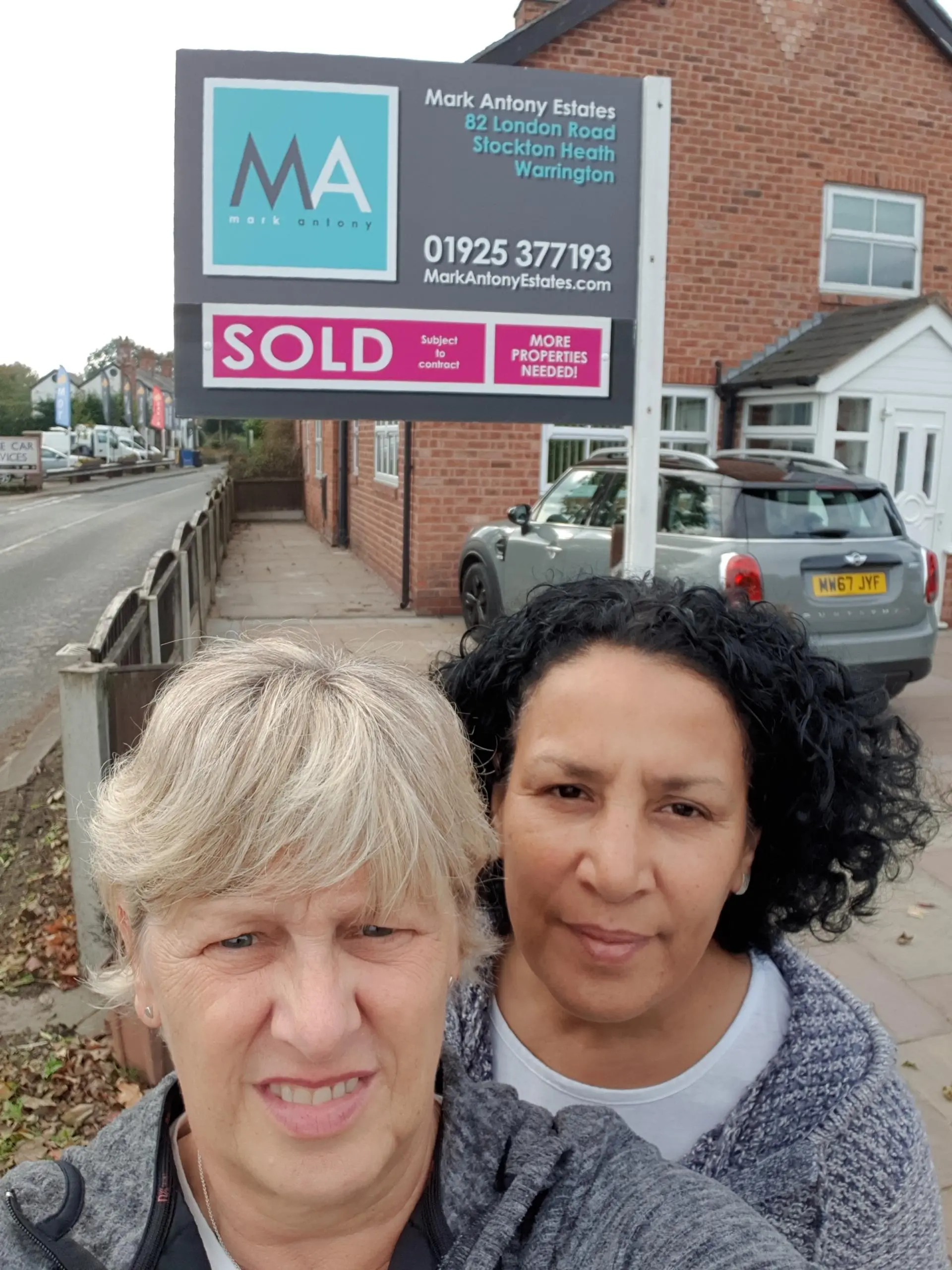 Two people posing in front of a Mark Antony Estates property board displaying "SOLD" in Stockton Heath, Warrington