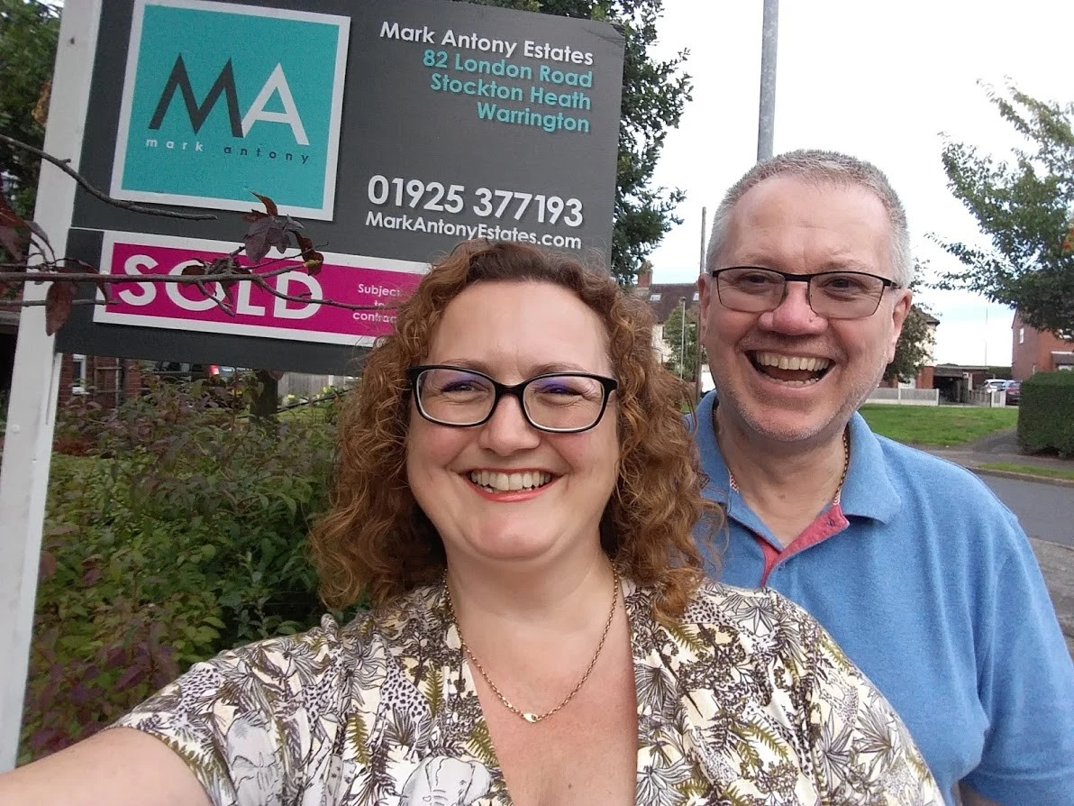 Two people smiling at camera in front of Mark Antony Estates property board showing sold status, 82 London Road, Stockton Heath, Warrington