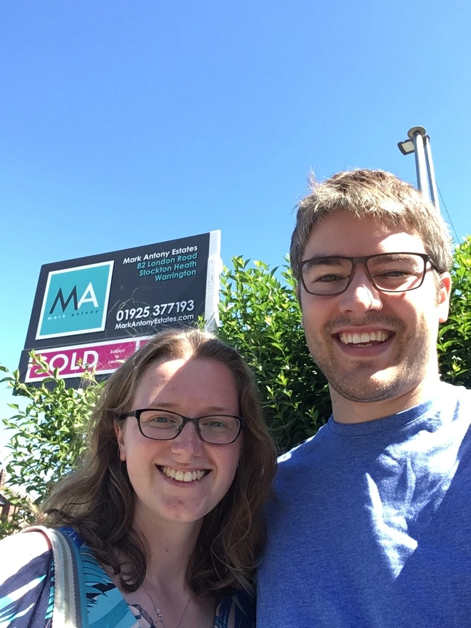Two people standing in front of a Mark Antony Estates property board marked "SOLD"