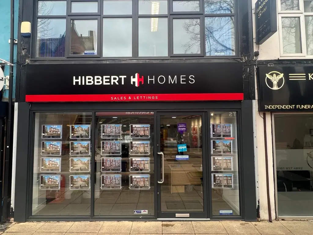 Hibbert Homes estate agency storefront with black fascia, red 'Sales & Lettings' banner, and property photographs displayed in windows