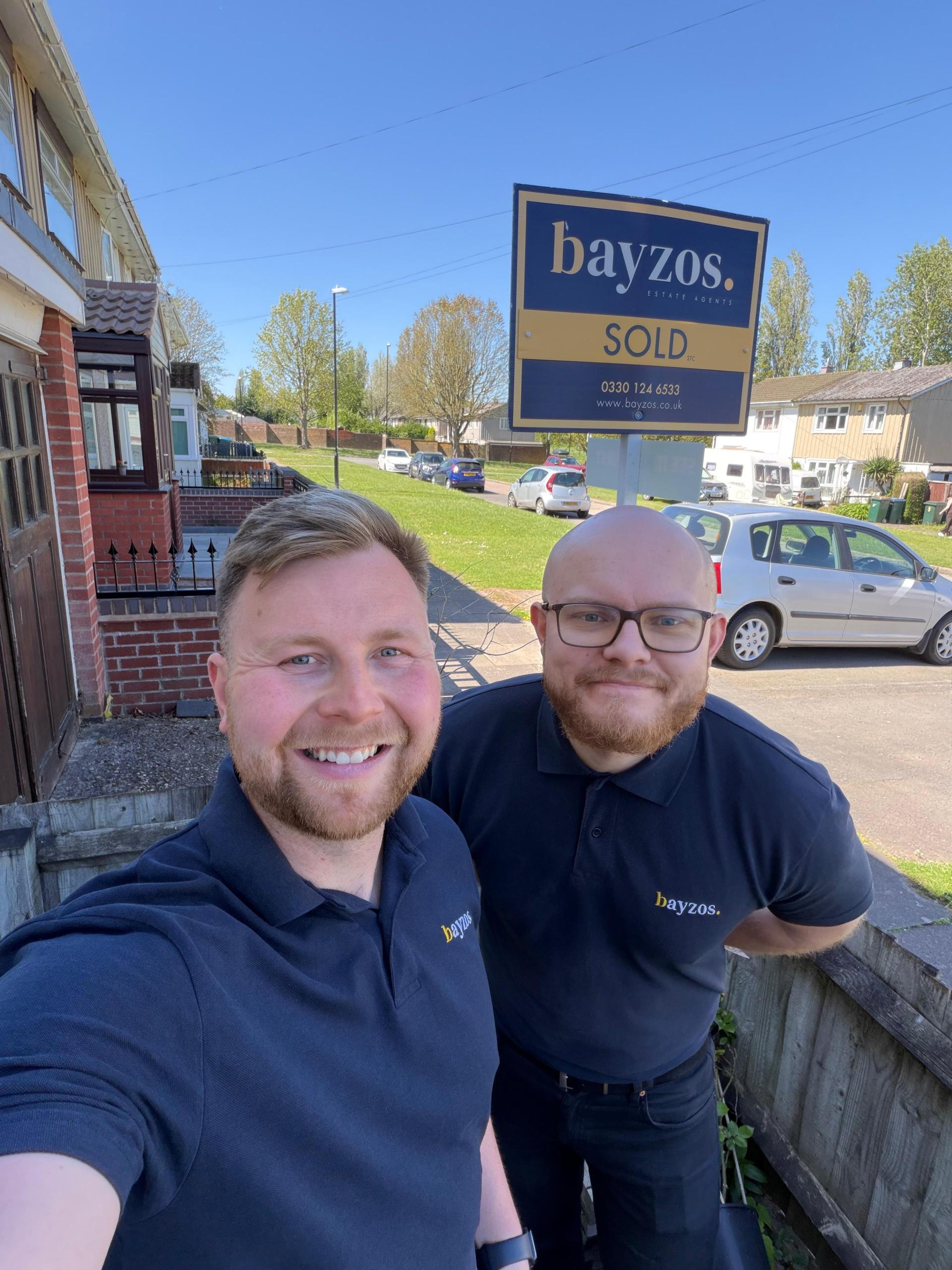 James stands with Jack, a viewing expert at bayzos estate agents. They stand in front of a house with a sold board outside