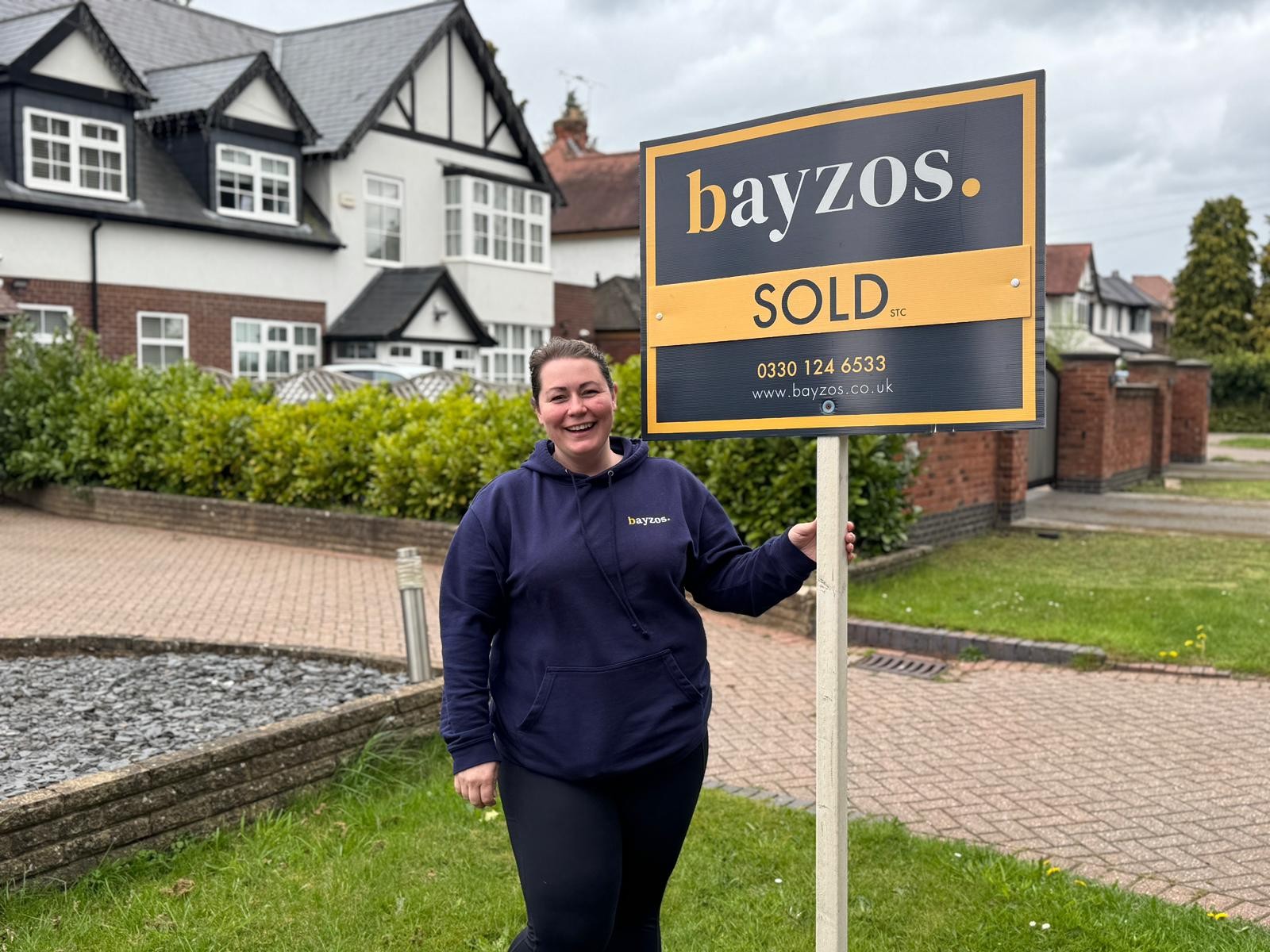 Caroline from Bayzos Estate Agents Coventry stands outside a property, next to a sold by Bayzos board