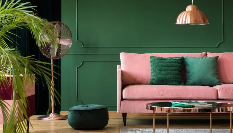 Interior living room with pink sofa, green panelled wall, copper pendant light, potted plant, and decorative accessories
