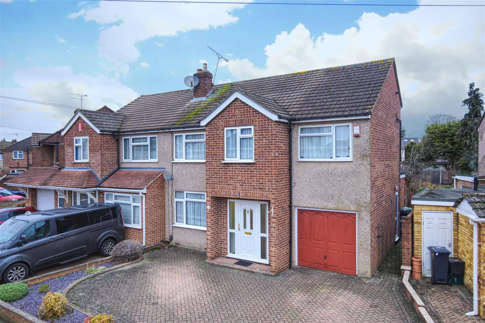 Semi-detached brick house with rendered sections, white-framed windows, red garage door, and driveway with parked car