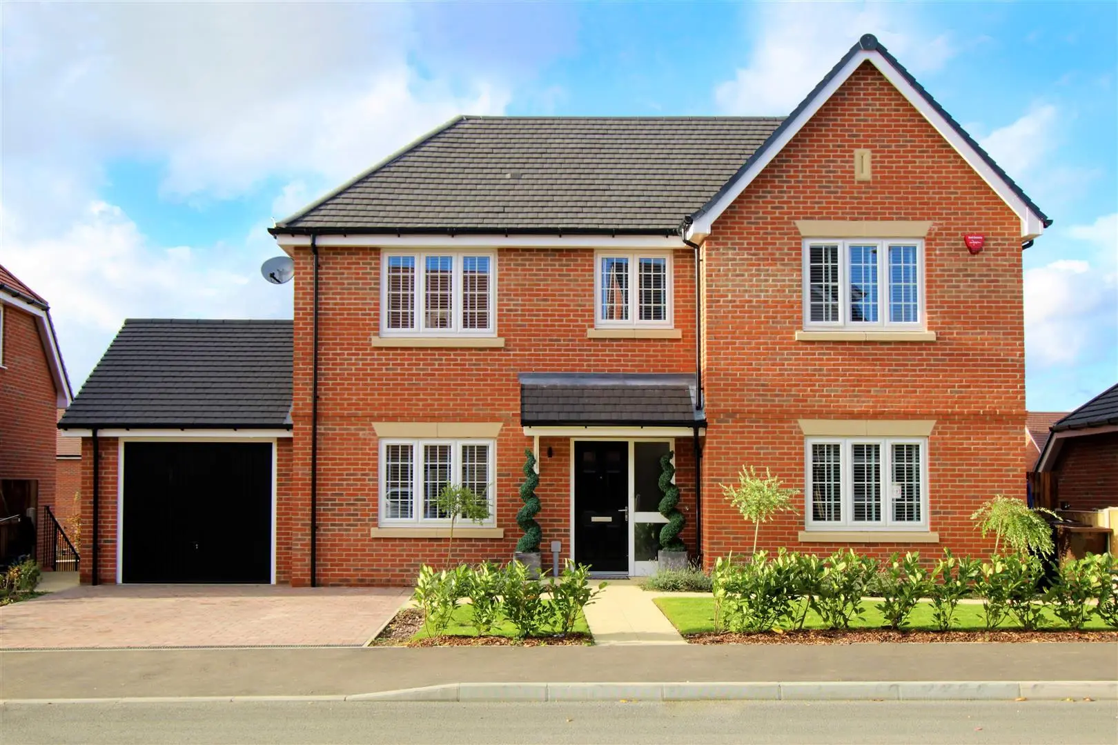 Red brick two-storey detached house with dark roof, garage, and landscaped front garden