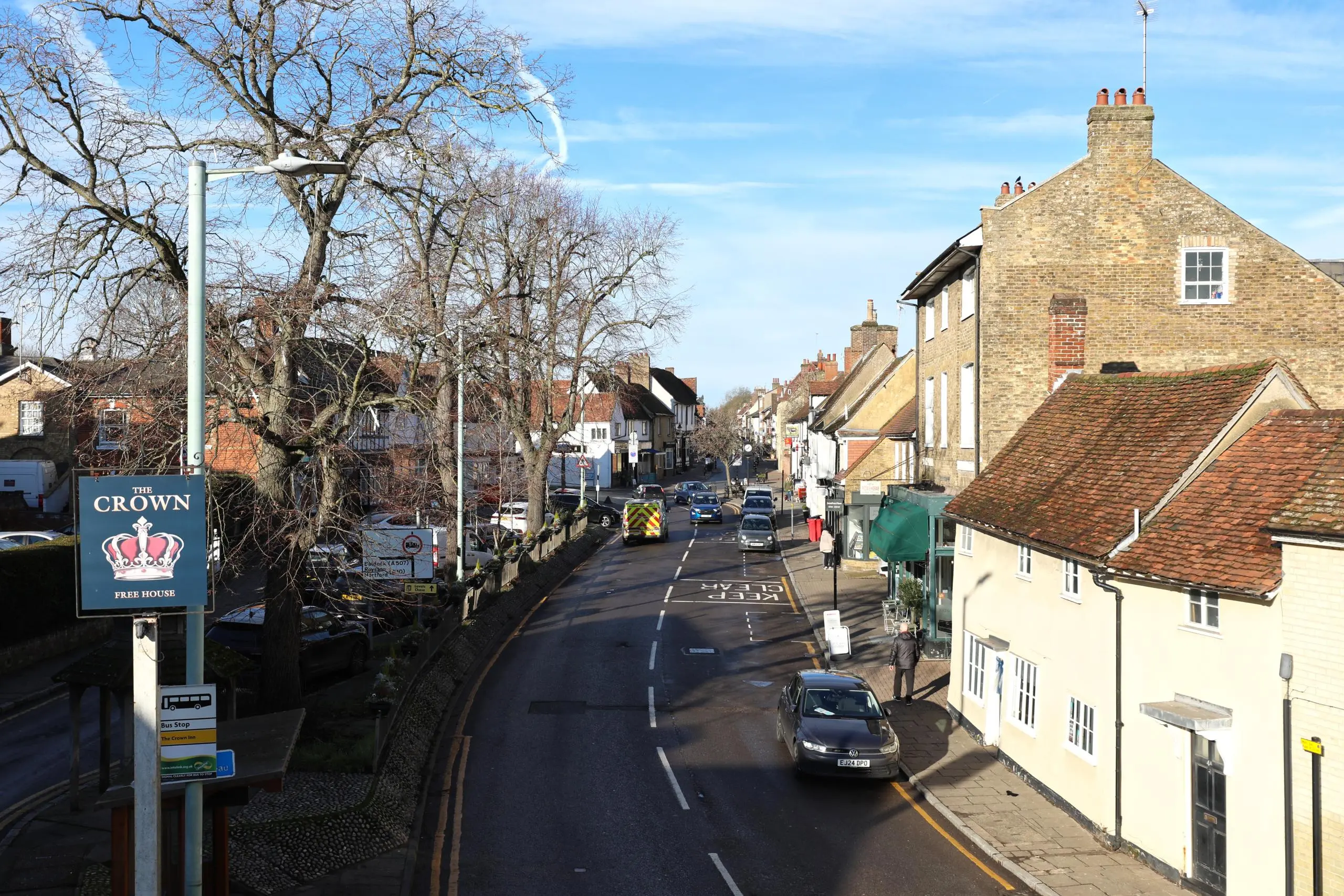 High street with period buildings, bare trees, parked cars, and a pub sign reading "The Crown Free House"
