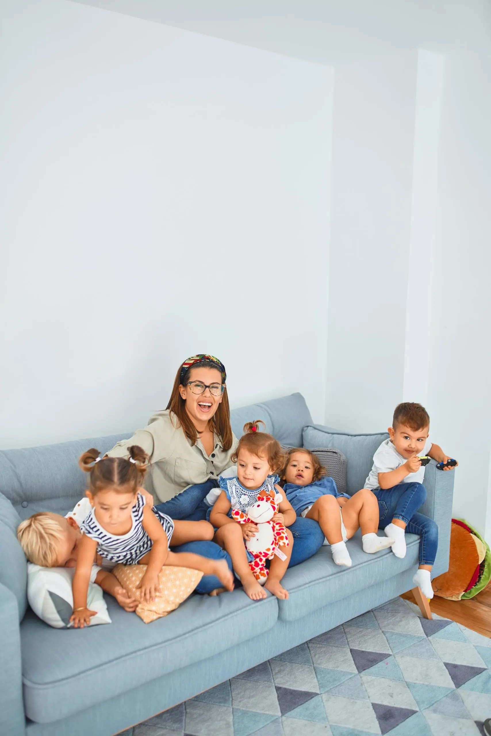 Woman and four young children sitting on a light blue sofa against a white wall