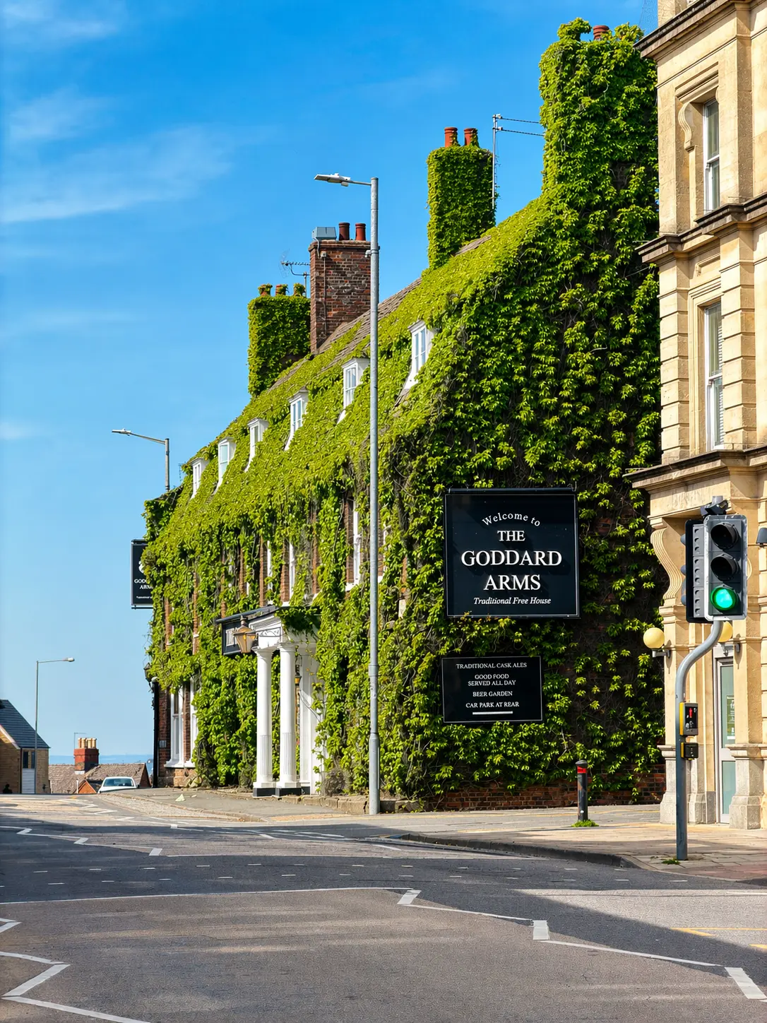 The Goddard Arms pub, a brick building covered in ivy with white-framed windows, a sign reading 'Welcome to THE GODDARD ARMS Traditional Free House' and details about traditional cask ales and beer garden