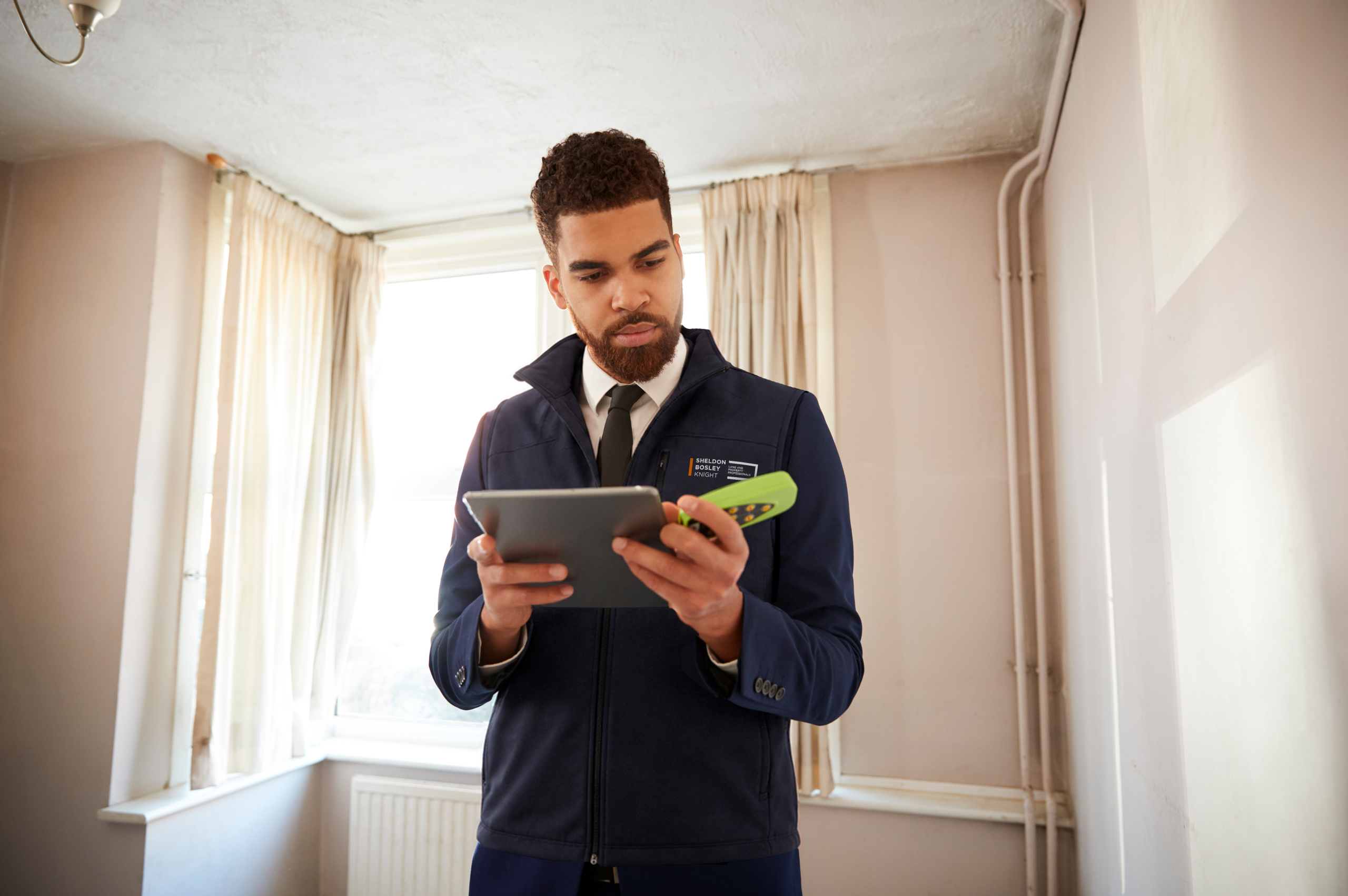 A valuer in a Sheldon Bosley Knight branded jacket is measuring a property