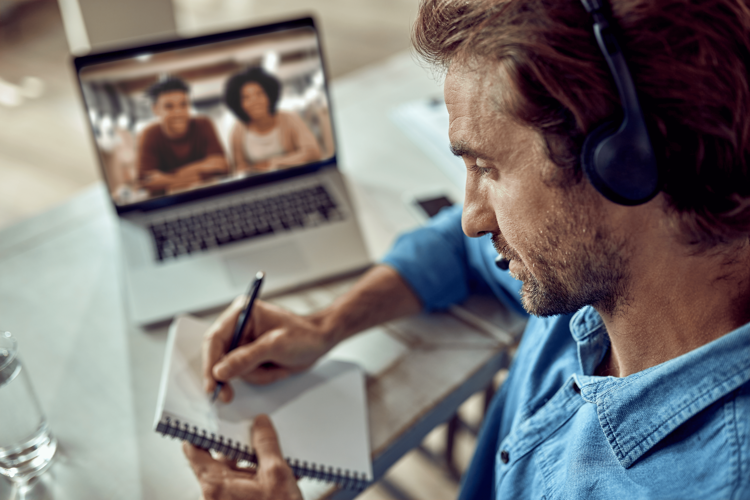 A man is on a zoom call with two homeowners and is taking notes