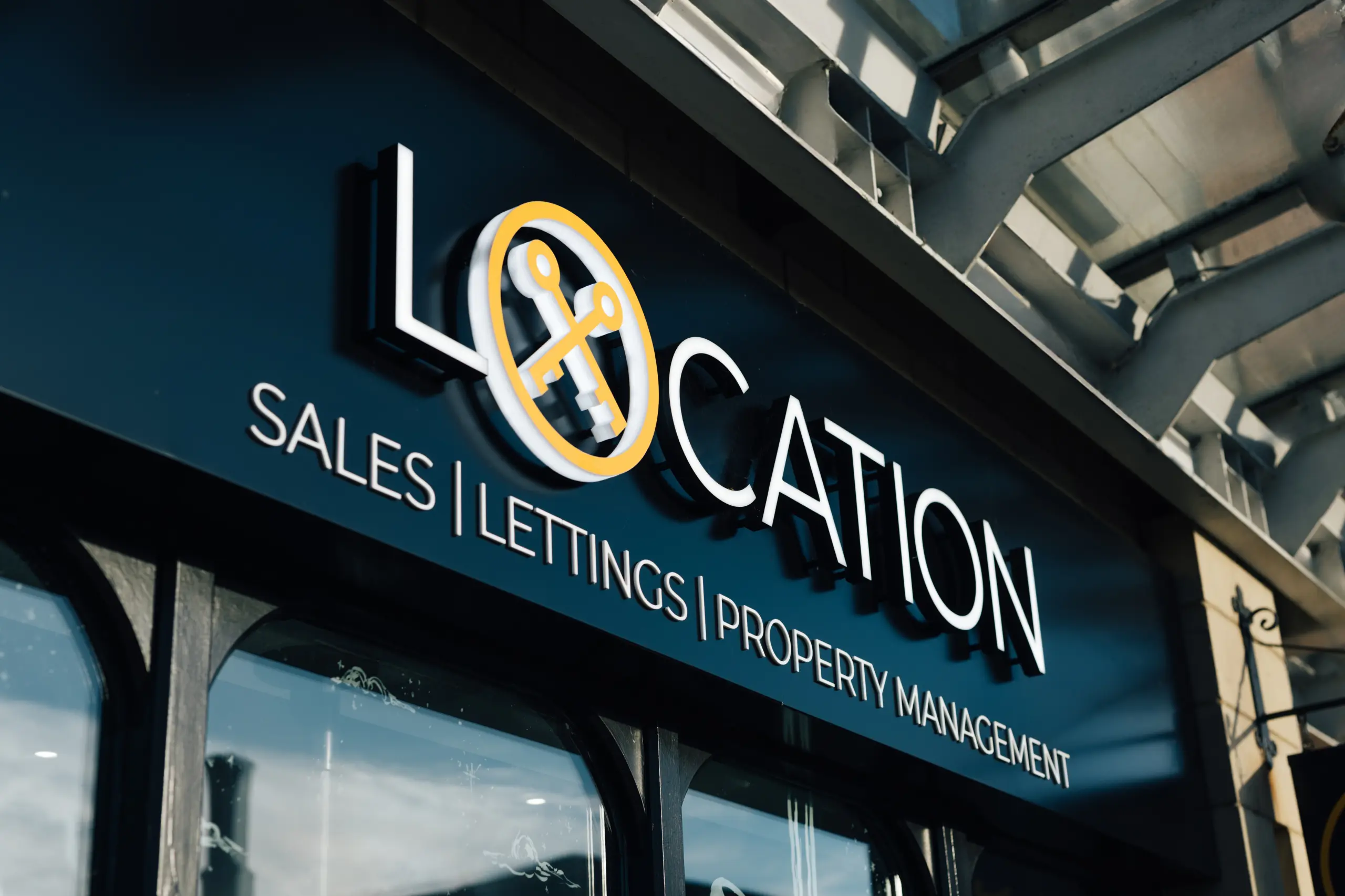 Location storefront sign reading 'Location Sales Lettings Property Management' with yellow and white logo on dark blue background