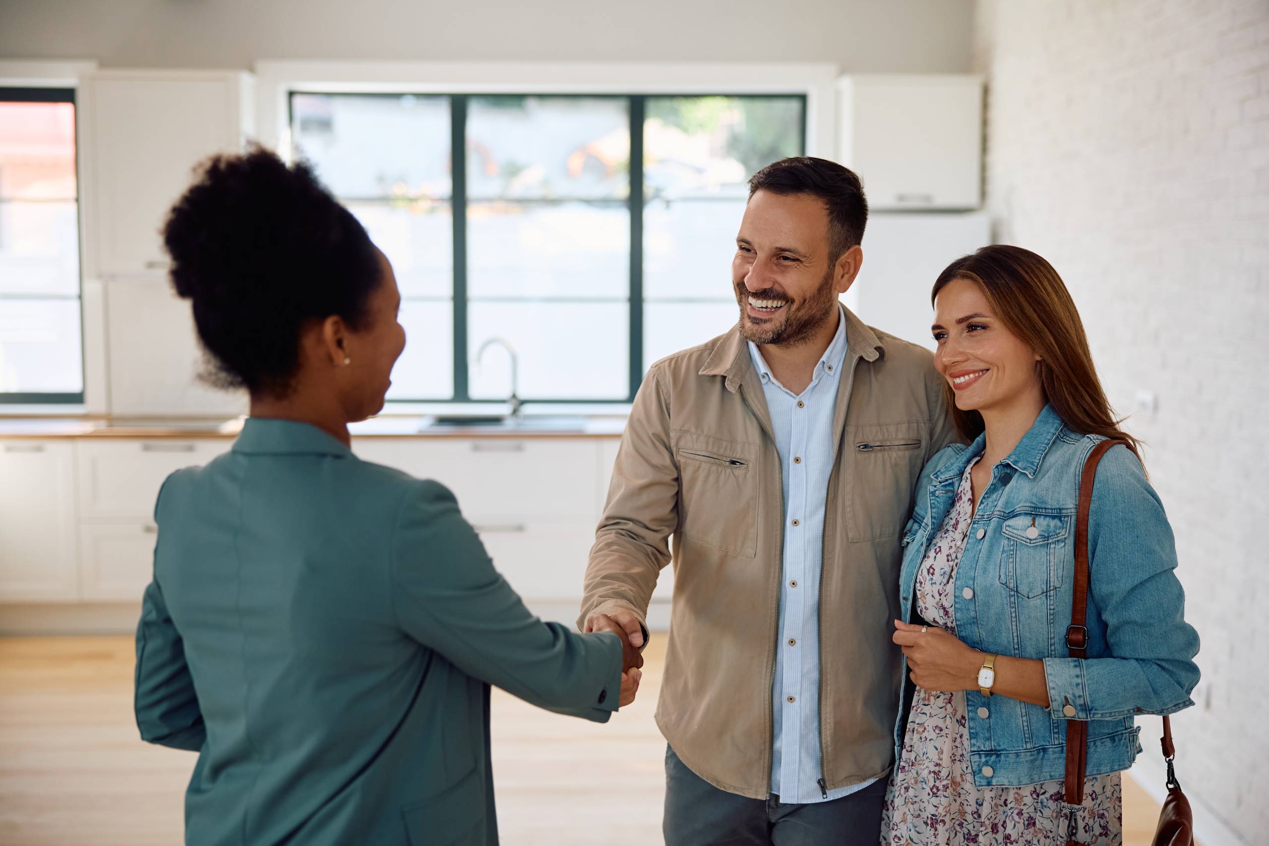 An estate agent shakes hands with a couple inside a house