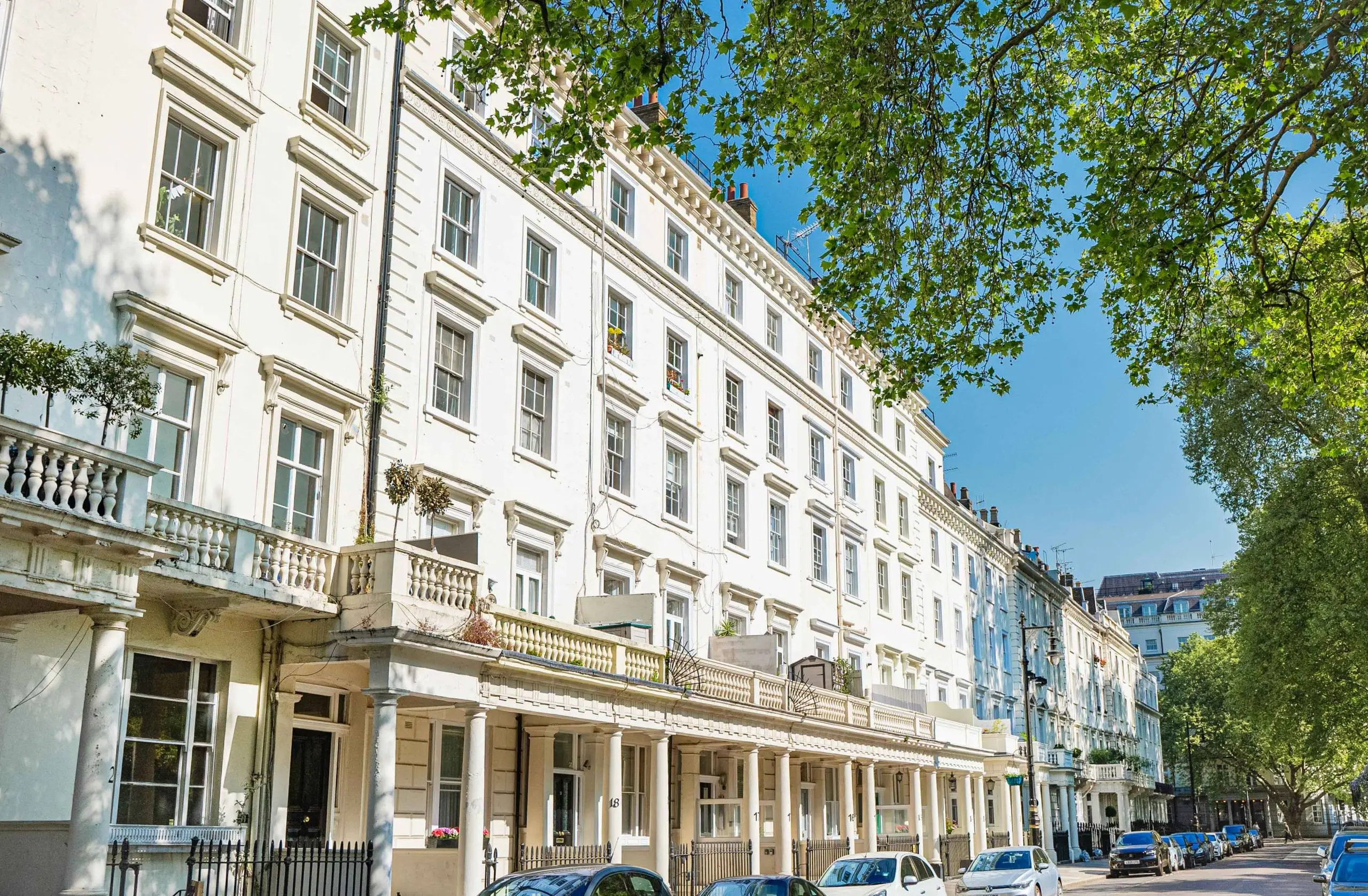 White stucco Georgian terraced building with sash windows, stone balustrade and columned ground-floor arcade, parked cars on street below