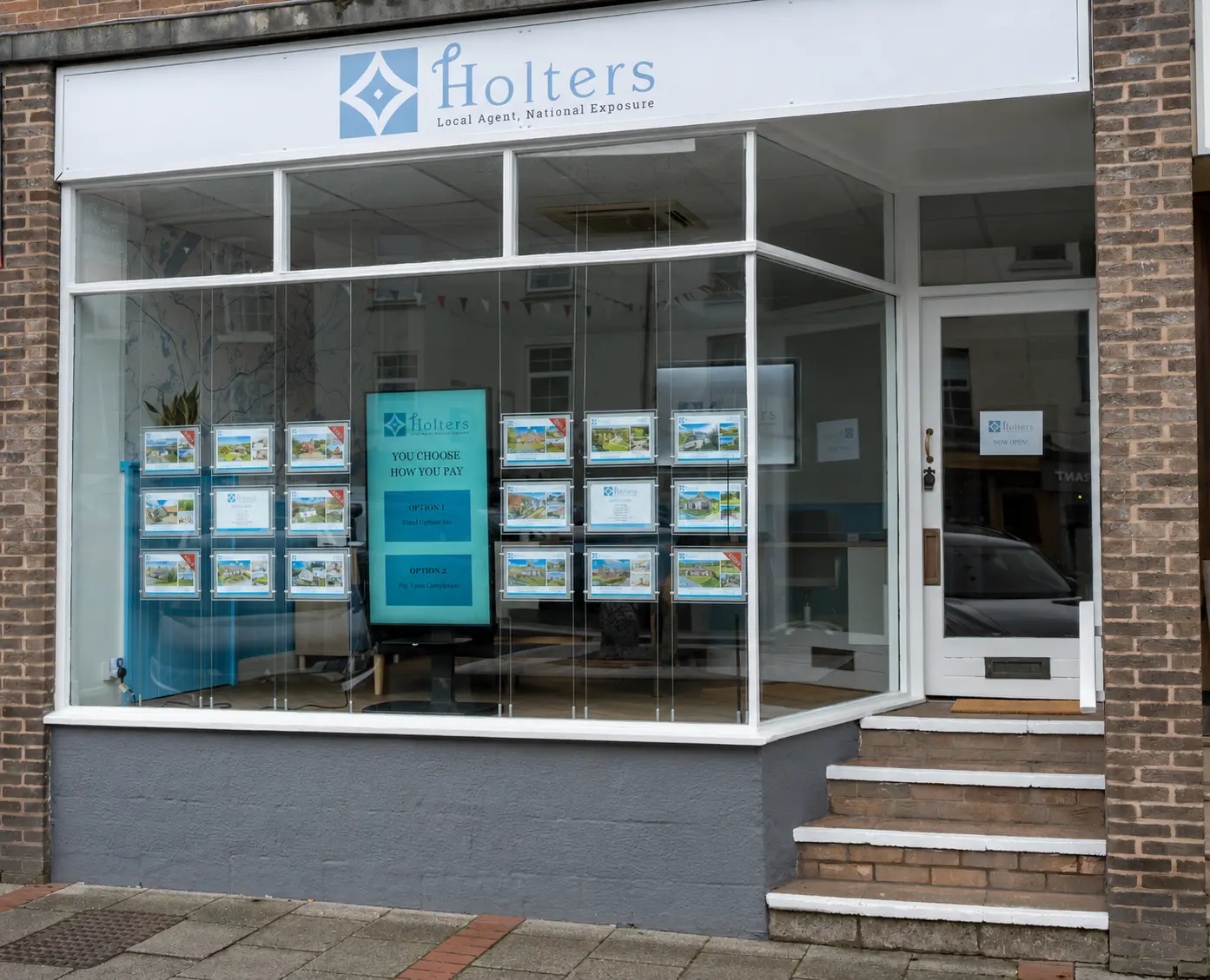 Holters estate agency storefront with white fascia, large windows displaying property listings, and turquoise interactive display panel