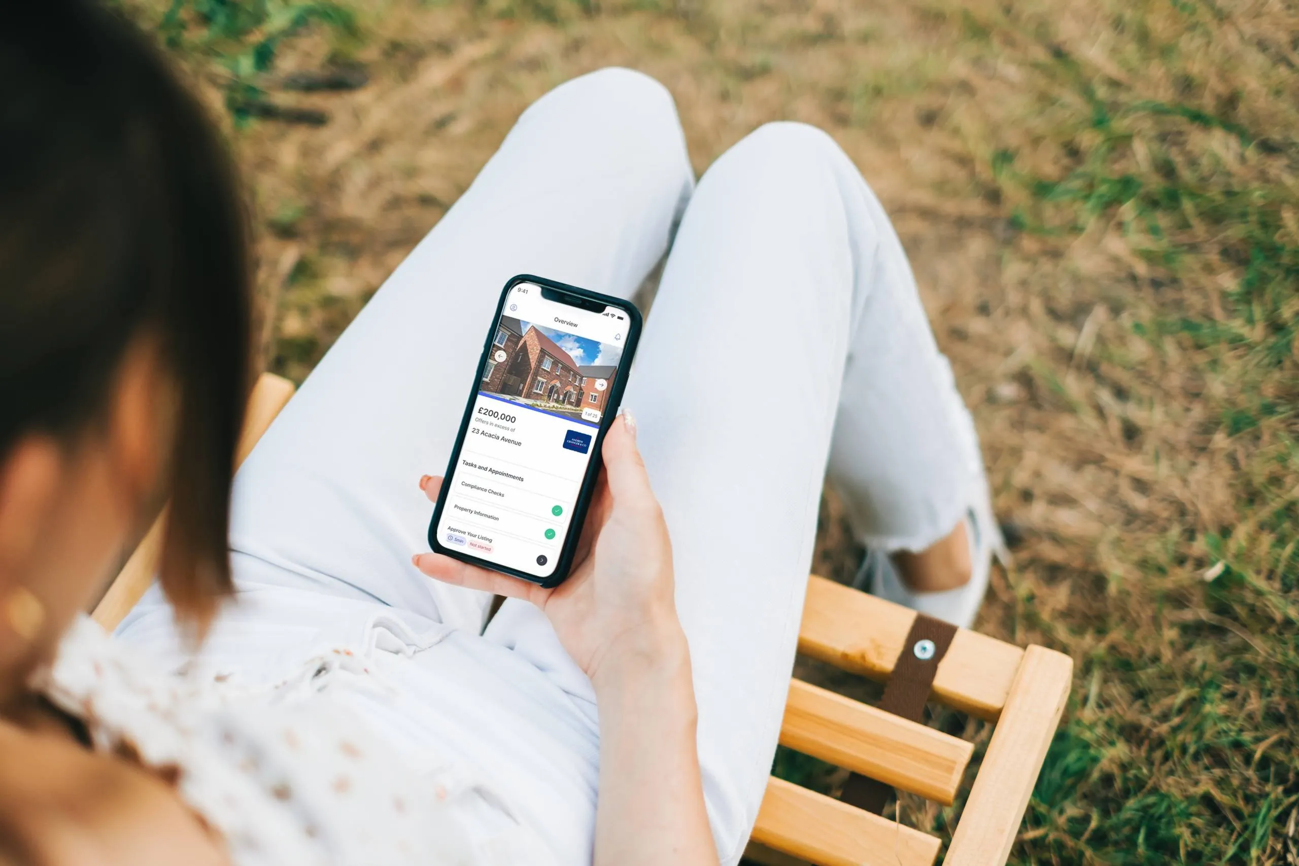 A woman sits on a bench looking at a property on the street buyer app