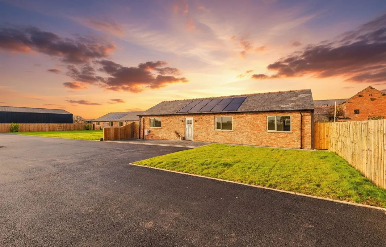Modern brick bungalow with solar panels on roof, driveway, lawn, and wooden fencing at sunset