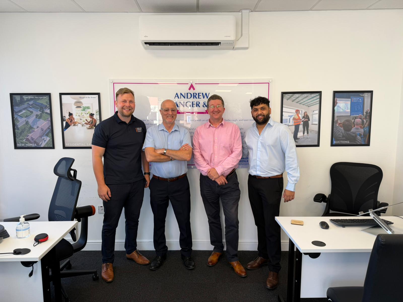 A group of Andrew Granger & Co's sales team stand in front of a branded sign