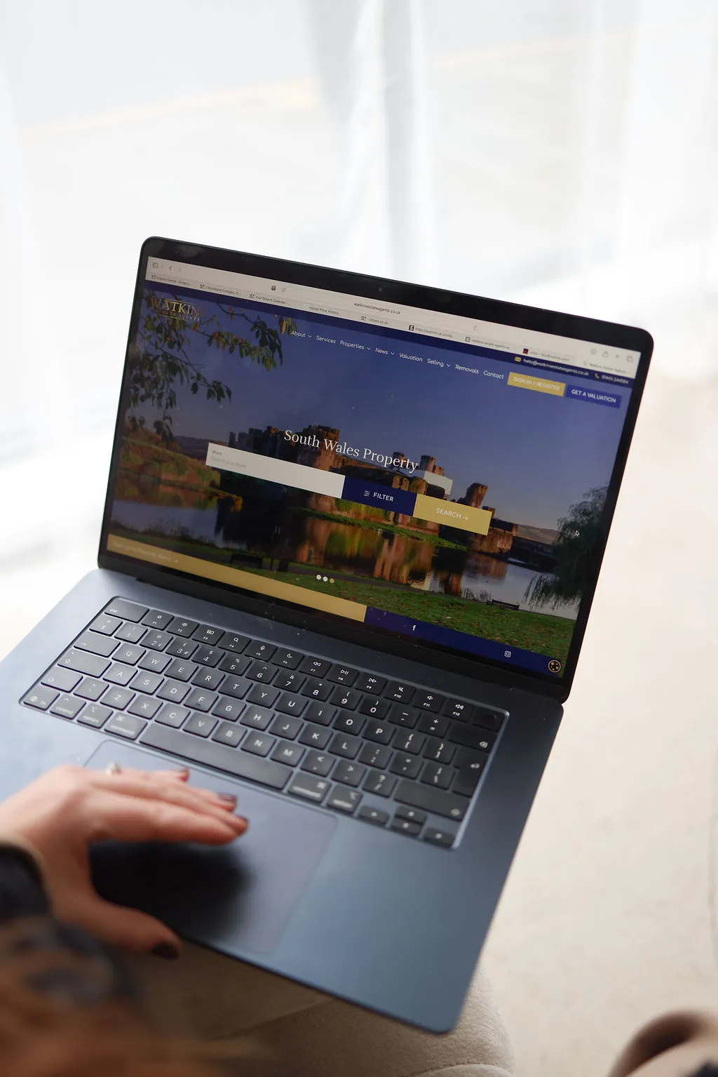 Laptop displaying Watkin Estate Agents website with "South Wales Property" heading and property search interface