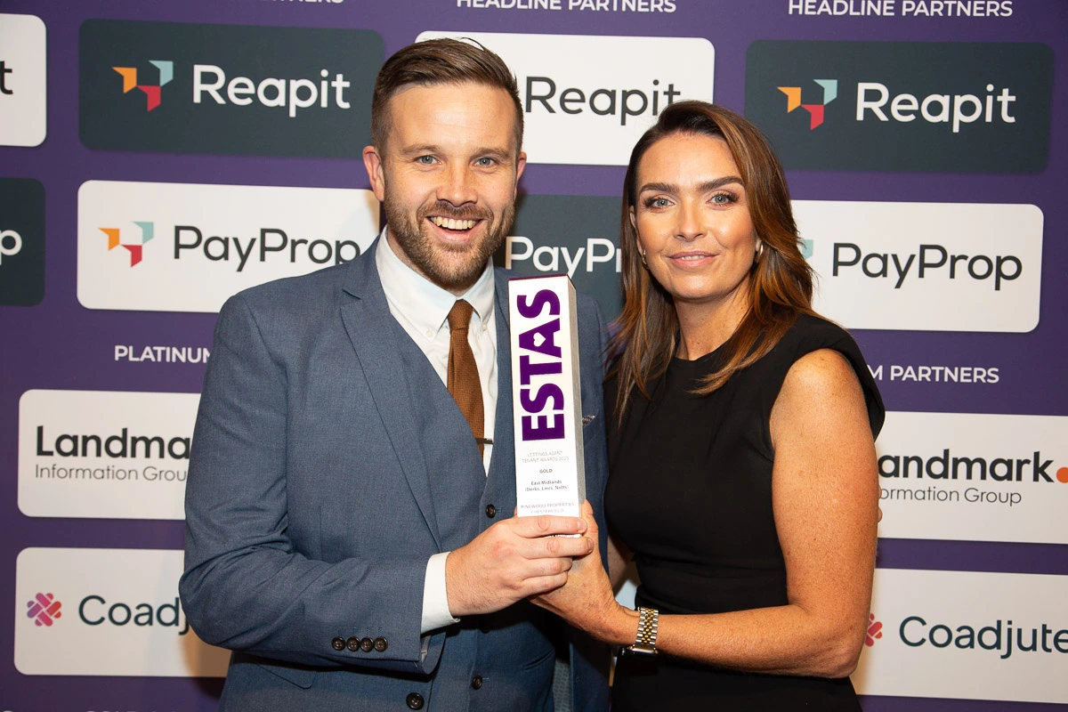 Two people holding an ESTAS award at a branded event backdrop featuring Reapit, PayProp, Landmark Information Group and Coadjute logos