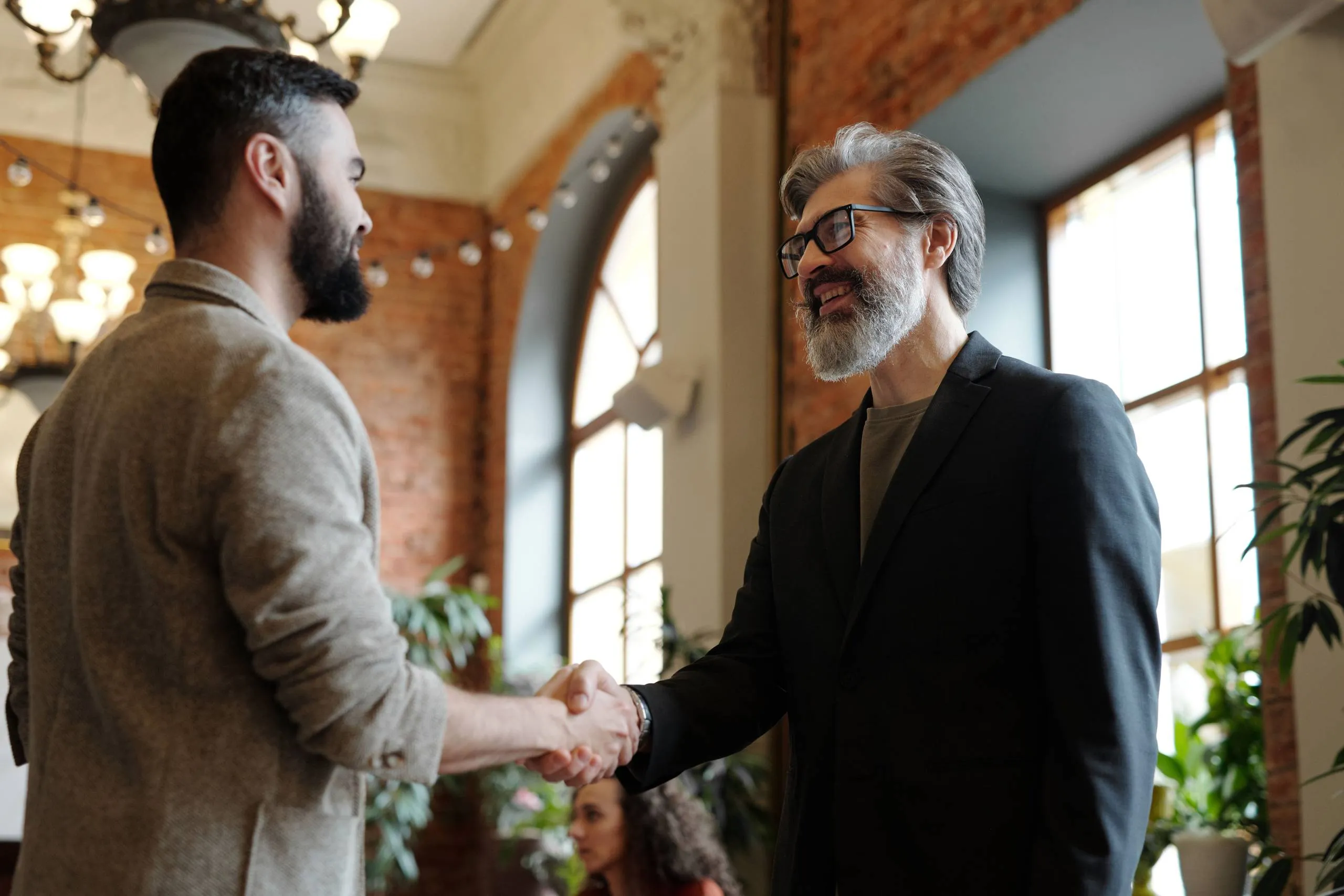 Two men shaking hands in a modern interior with exposed brick walls and large windows