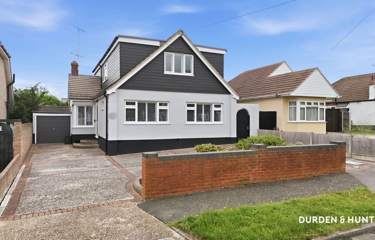 White and black rendered bungalow with dark tiled roof, dormer window, driveway and brick boundary wall