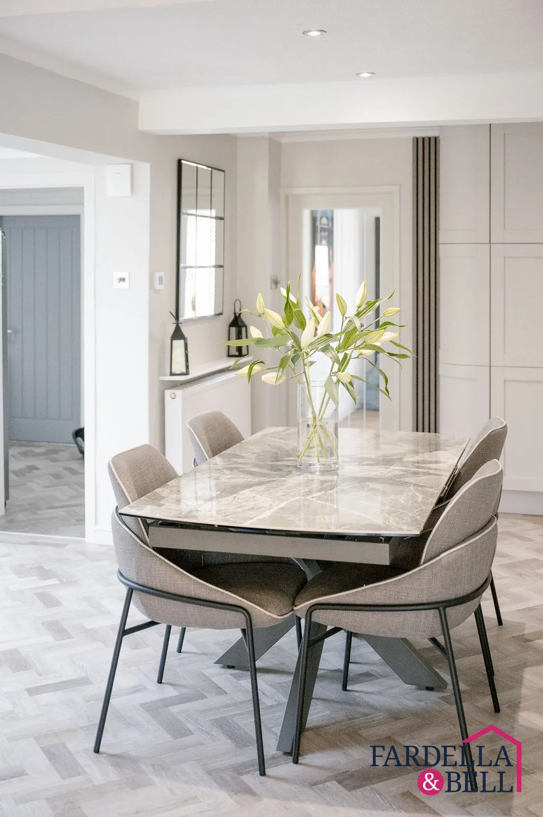 Modern dining room with marble-topped table, four upholstered chairs, fresh flowers in a vase, and a mirror on the wall