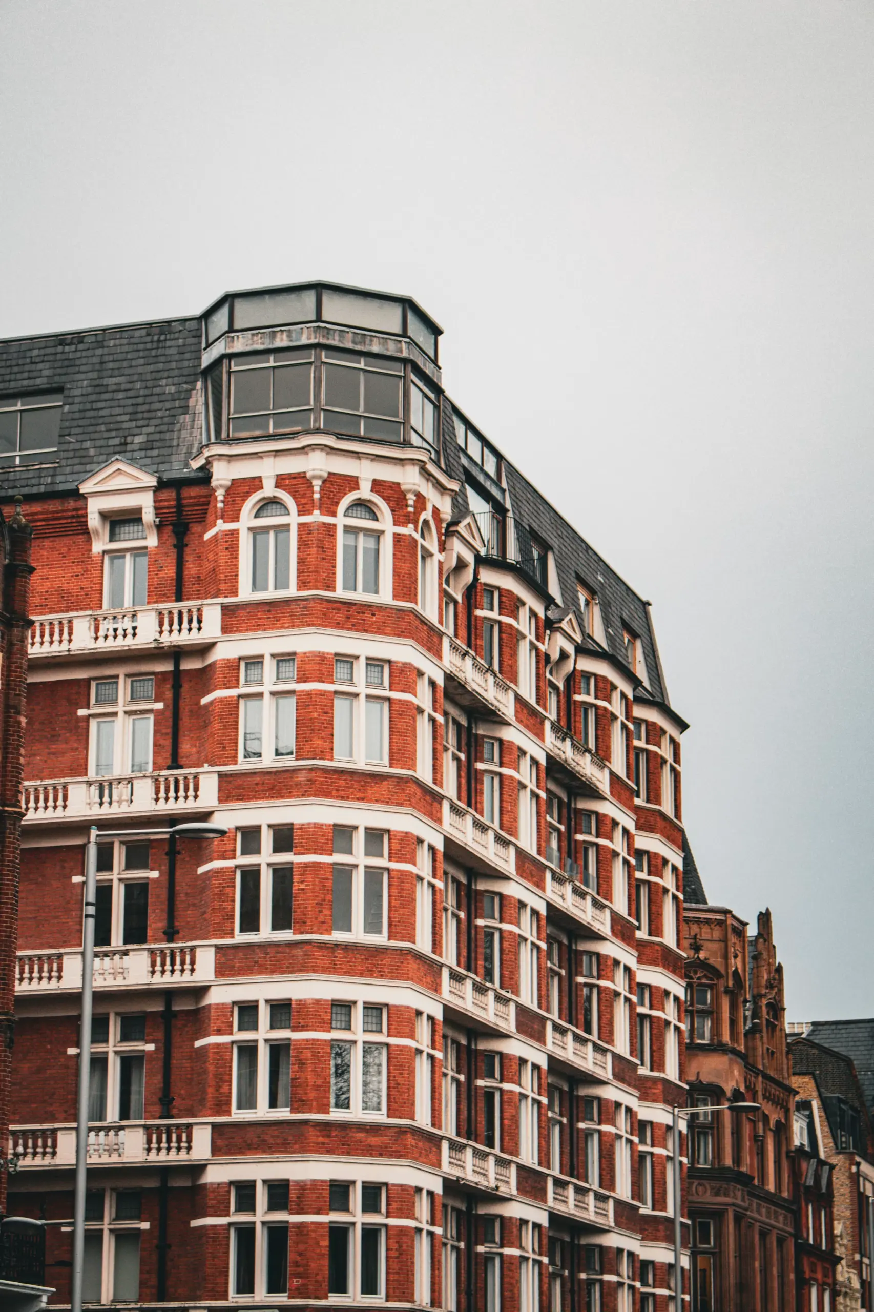 Victorian red brick building with white stone detailing, curved corner facade, ornate balustrades, and multi-pane windows