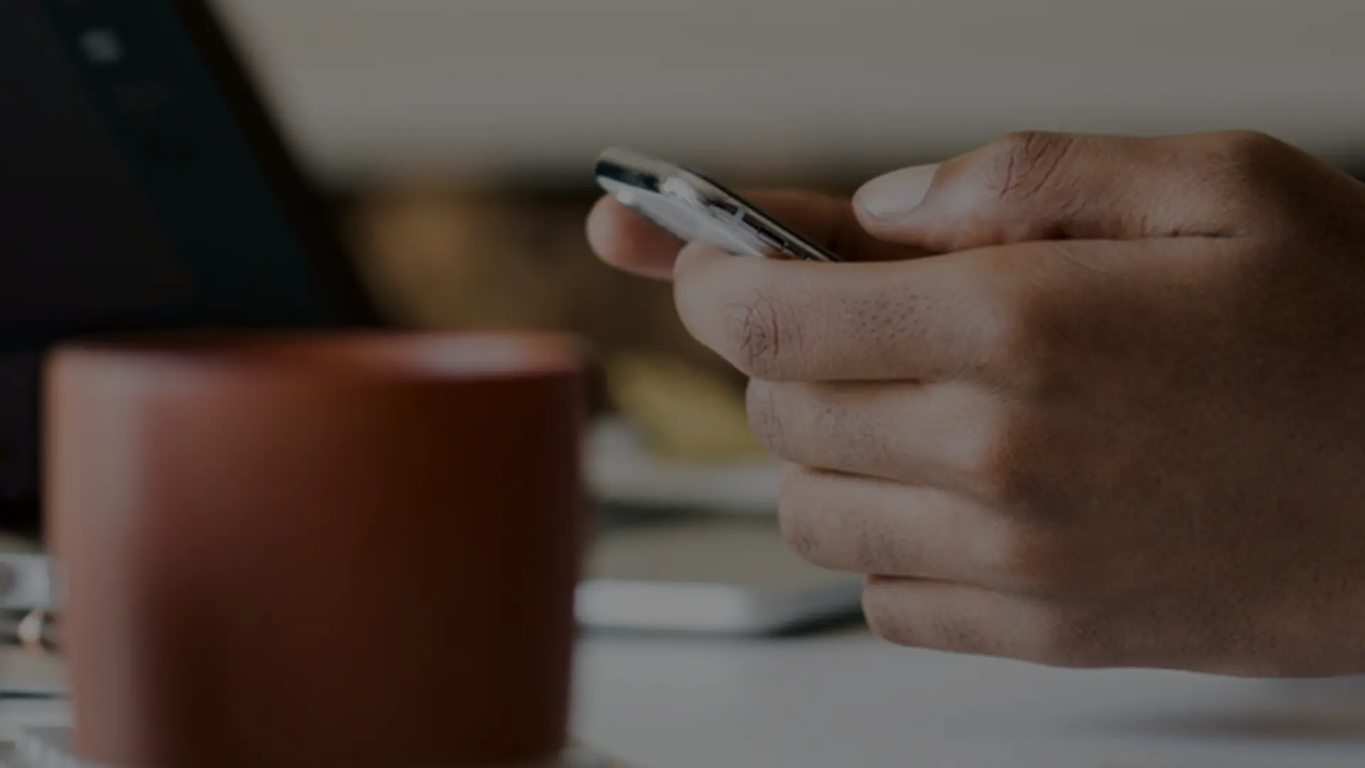Hand holding a smartphone with a cup in the background