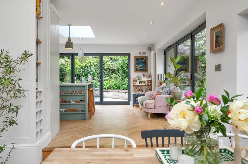 Bright open-plan living room with bi-fold doors onto a garden, pink armchair and fresh flowers — McCallum Marsh Services page, Market Harborough