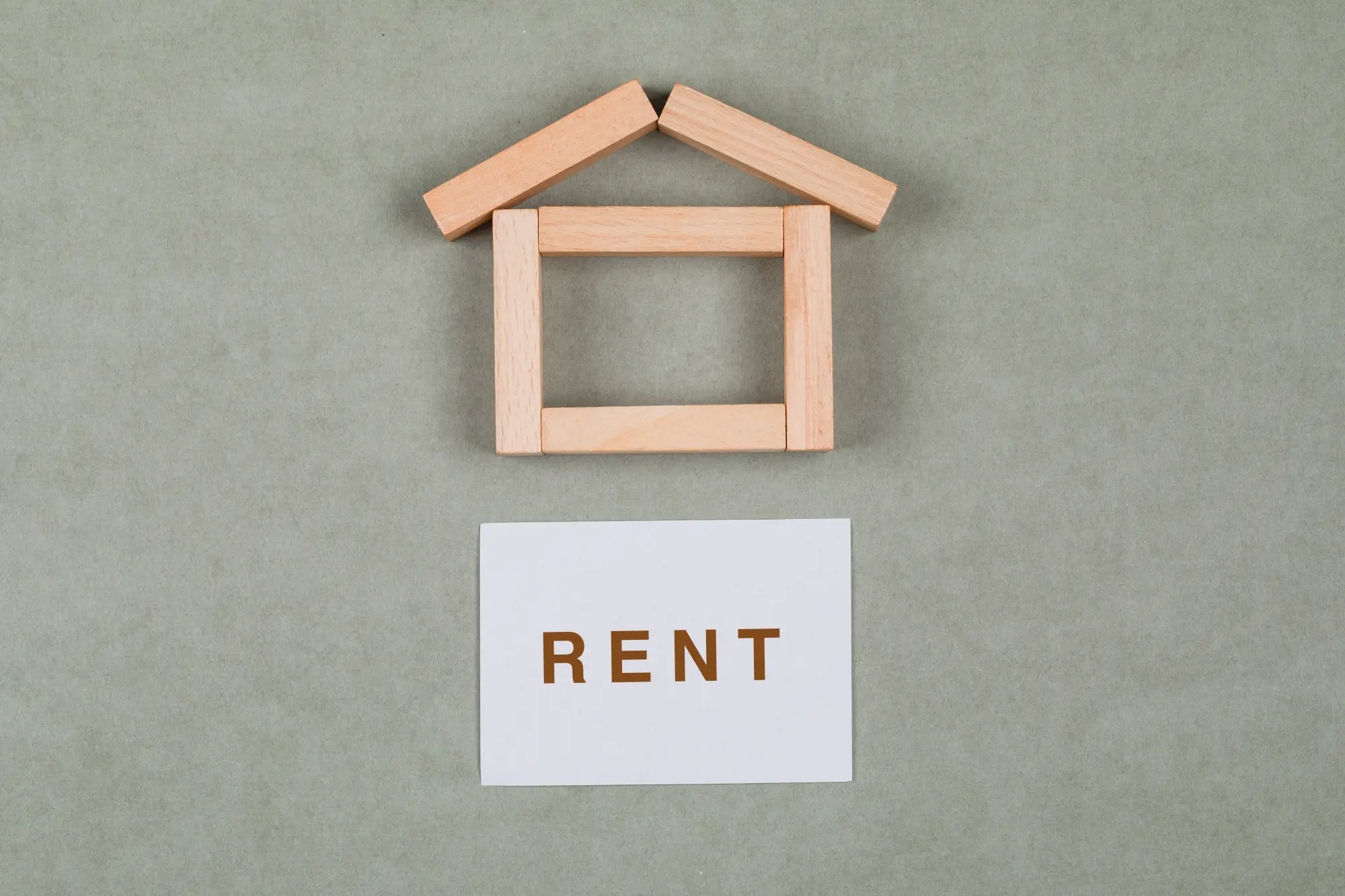 Wooden house-shaped blocks above a white card printed with the word RENT