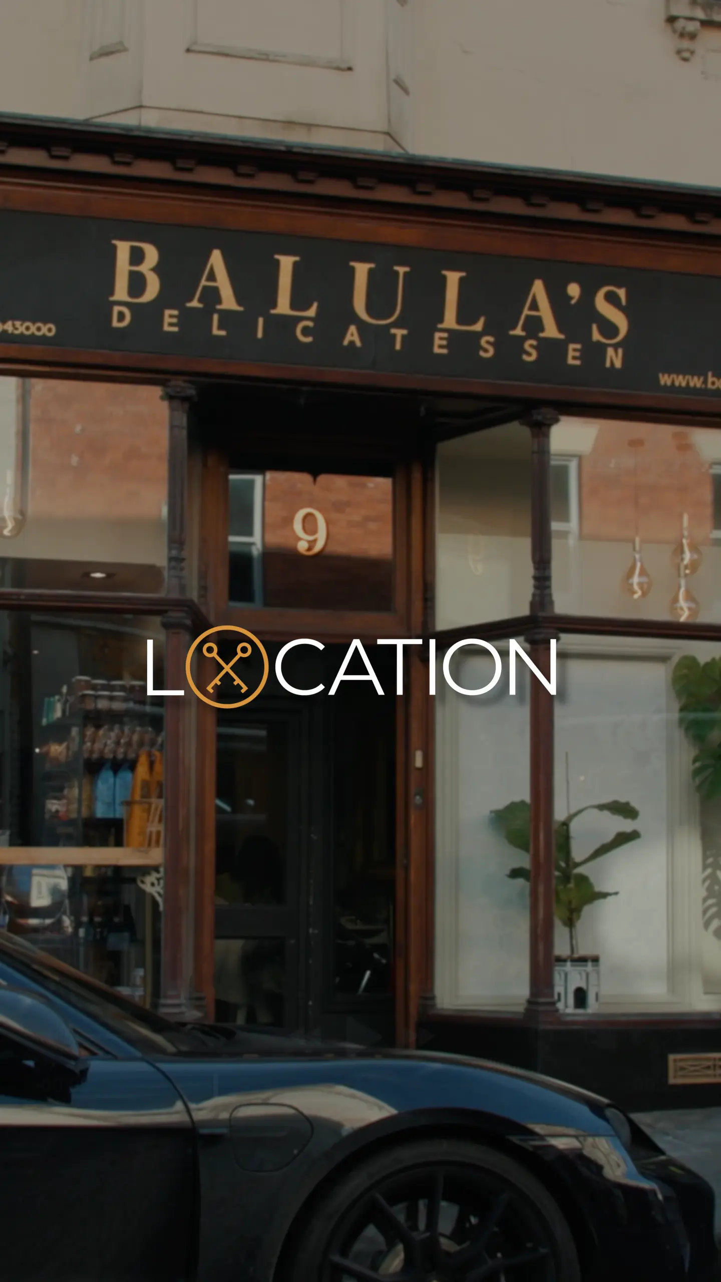 Storefront of Balula's Delicatessen with dark wood framing, number 9 on the door, and potted plants in the window