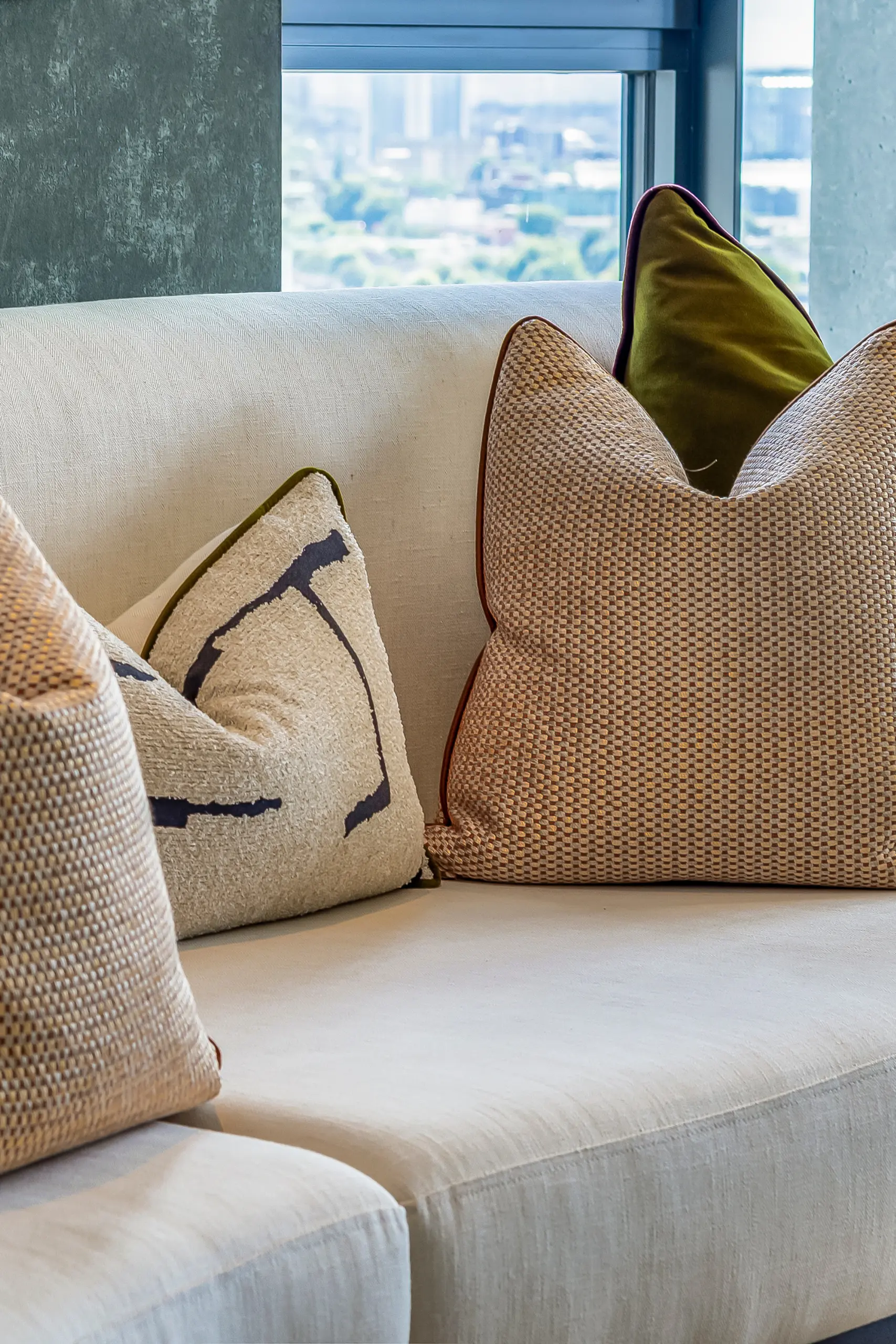 Cream sofa with olive green and patterned cushions, floor-to-ceiling window overlooking cityscape