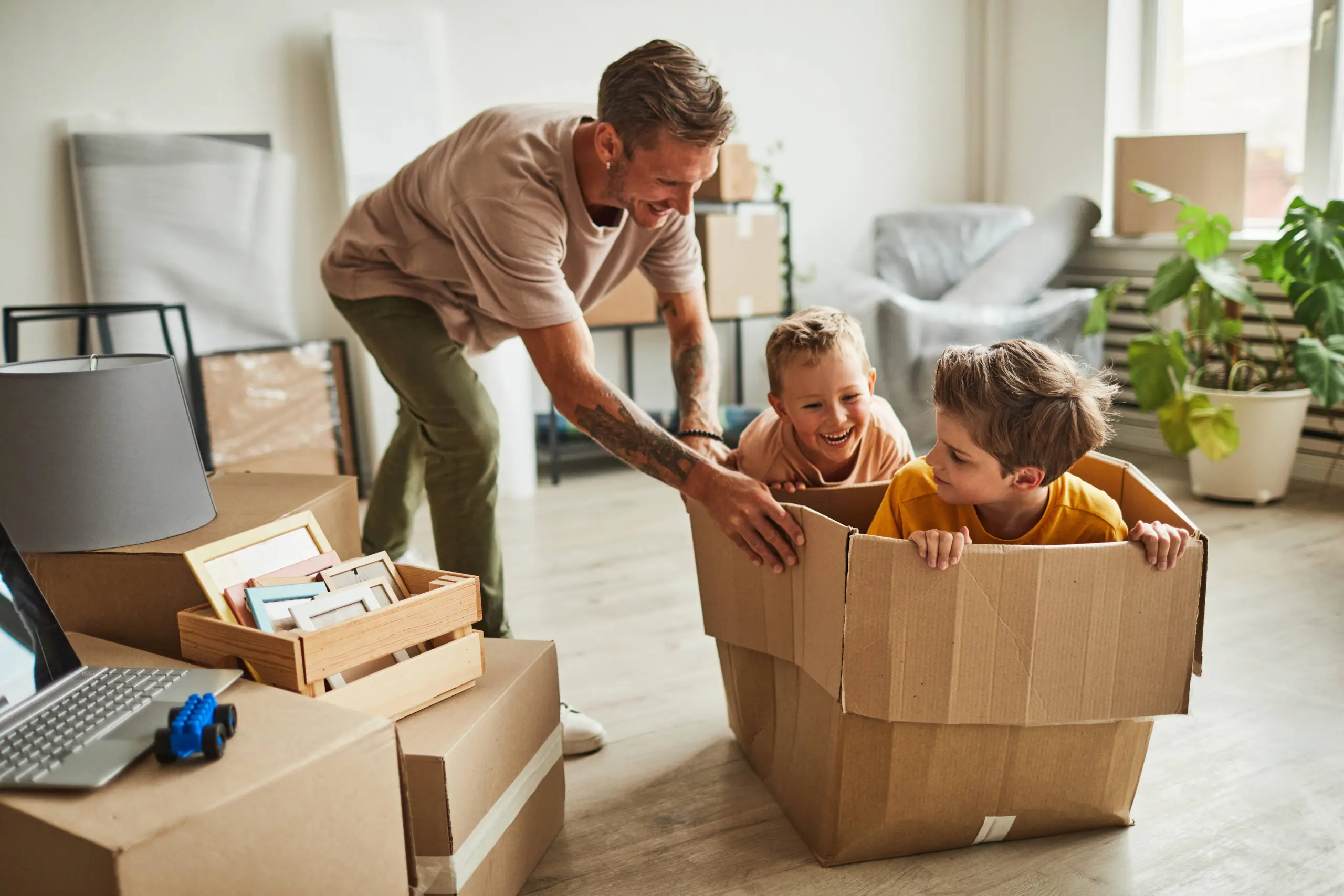 A man playing with two children in a cardboard box in a house